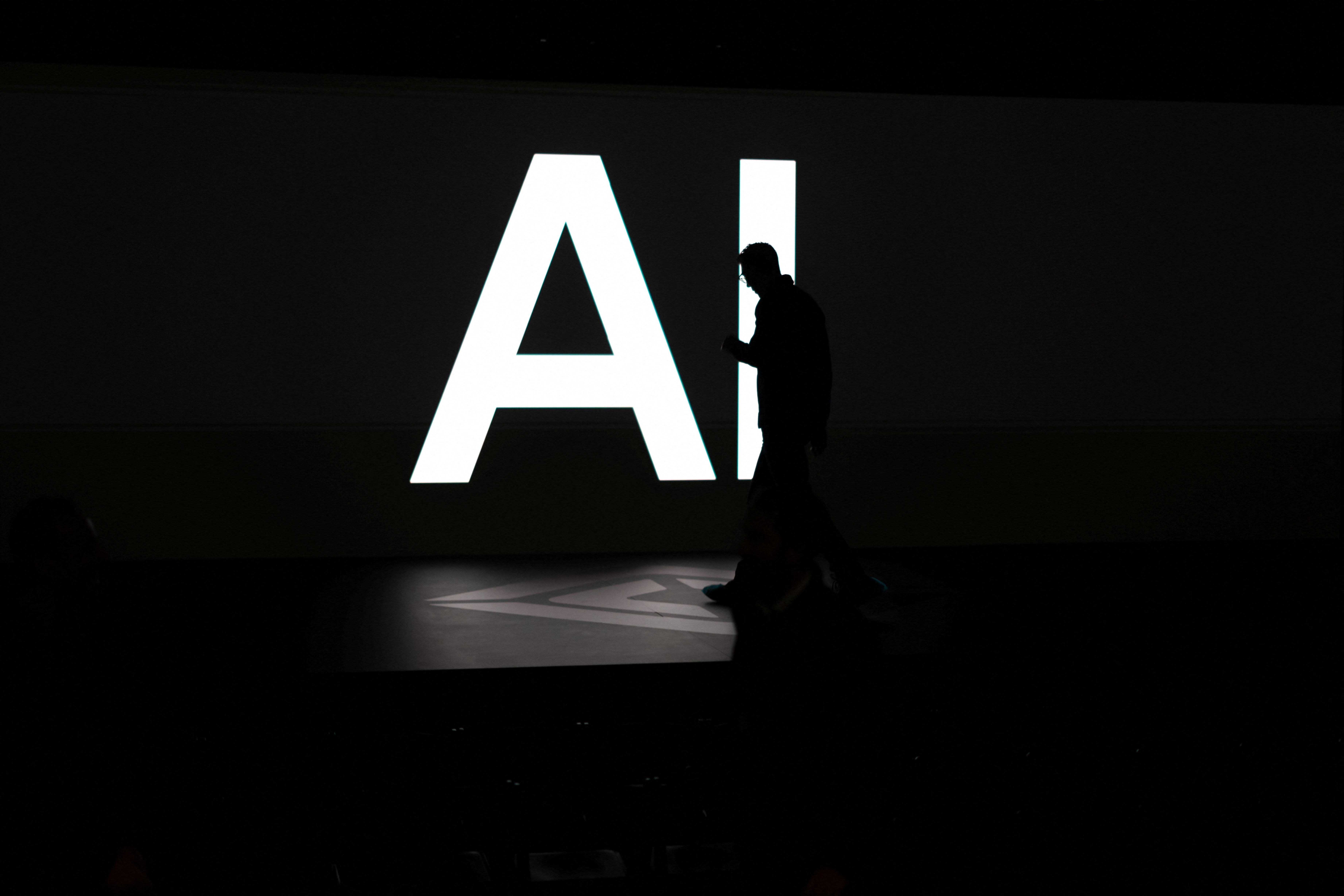 A screen reads “AI” as attendees gather during Rivian’s first Autonomy and AI Day in Palo Alto