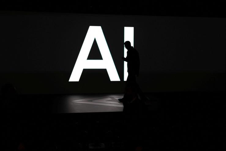A screen reads “AI” as attendees gather during Rivian’s first Autonomy and AI Day in Palo Alto