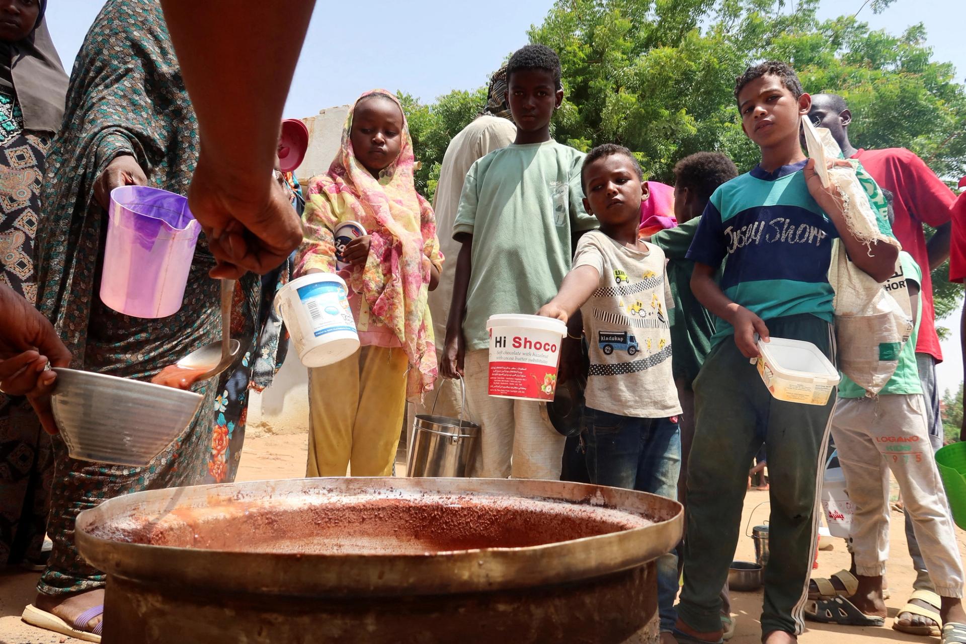 People hold pots as volunteers distribute food in Omdurman, Sudan.