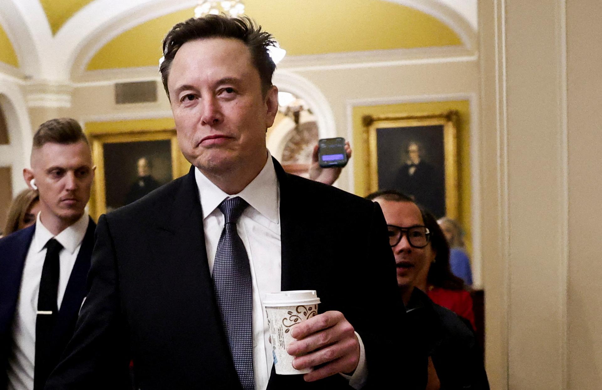 Elon Musk walks on Capitol Hill holding a cup of coffee.