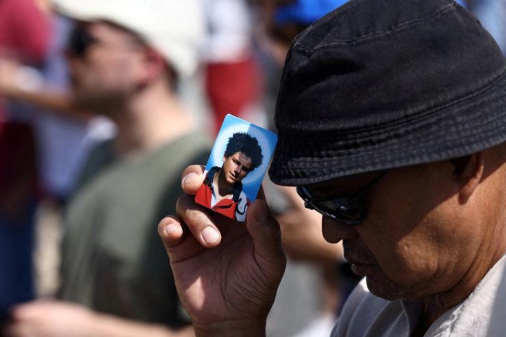 A man prays while holding a photo of Carlo Acutis.