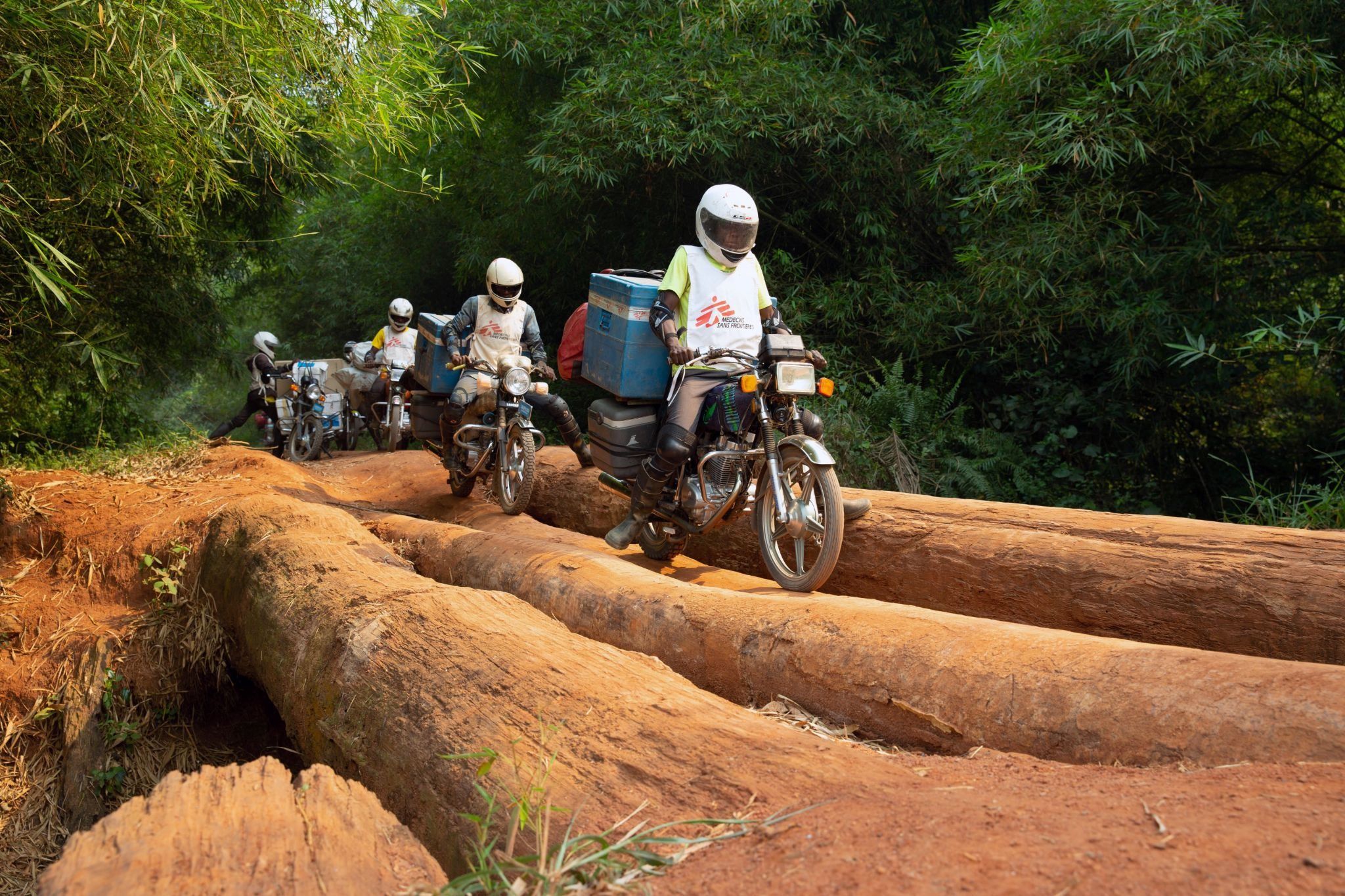 A motorcycle convoy carrying vials of measles vaccine and other supplies for medial NGO Doctors Without Borders (MSF) crosses a log bridge.