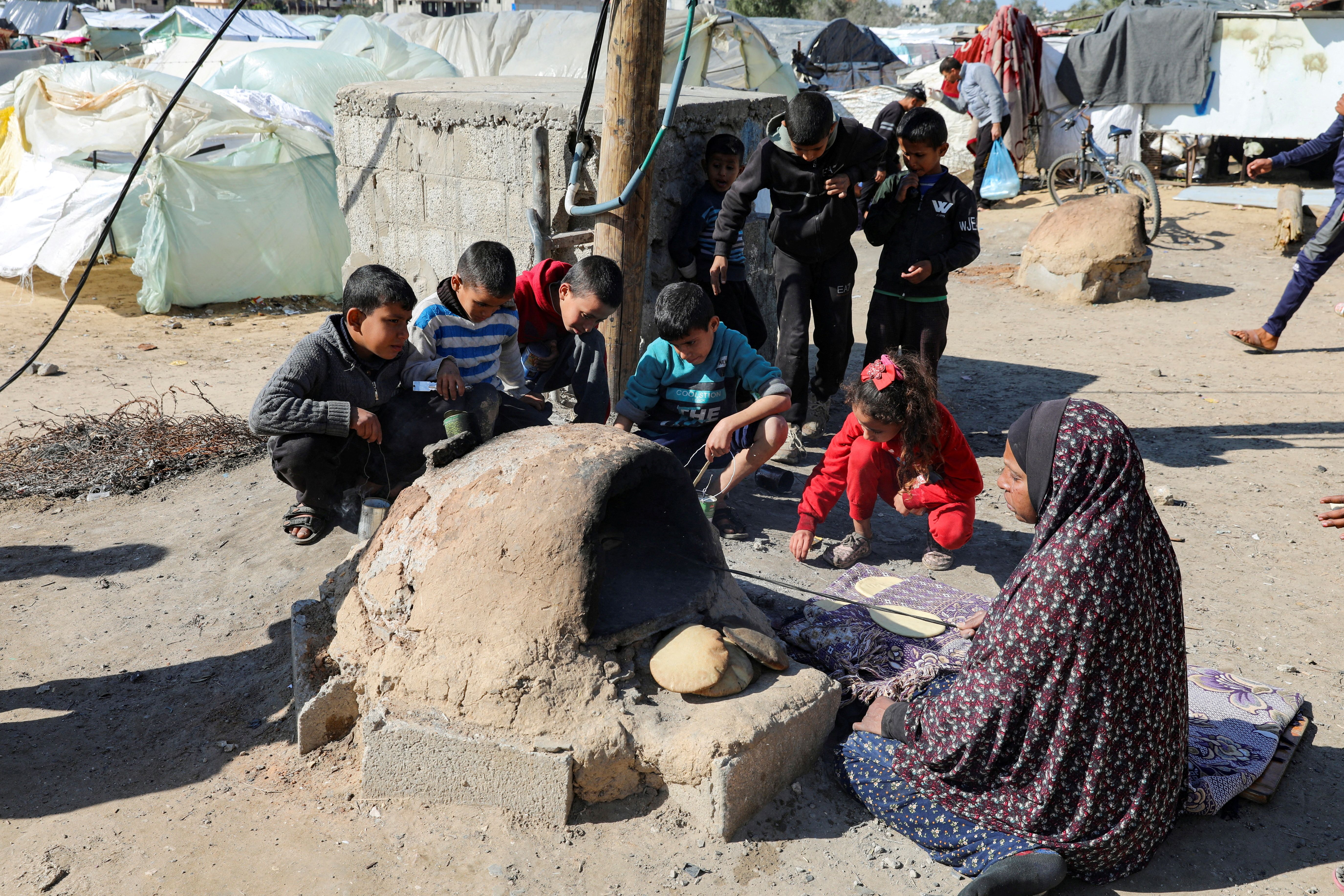 A Palestinian woman bakes bread as children sit next to her, while Gaza residents face crisis levels of hunger and soaring malnutrition.
