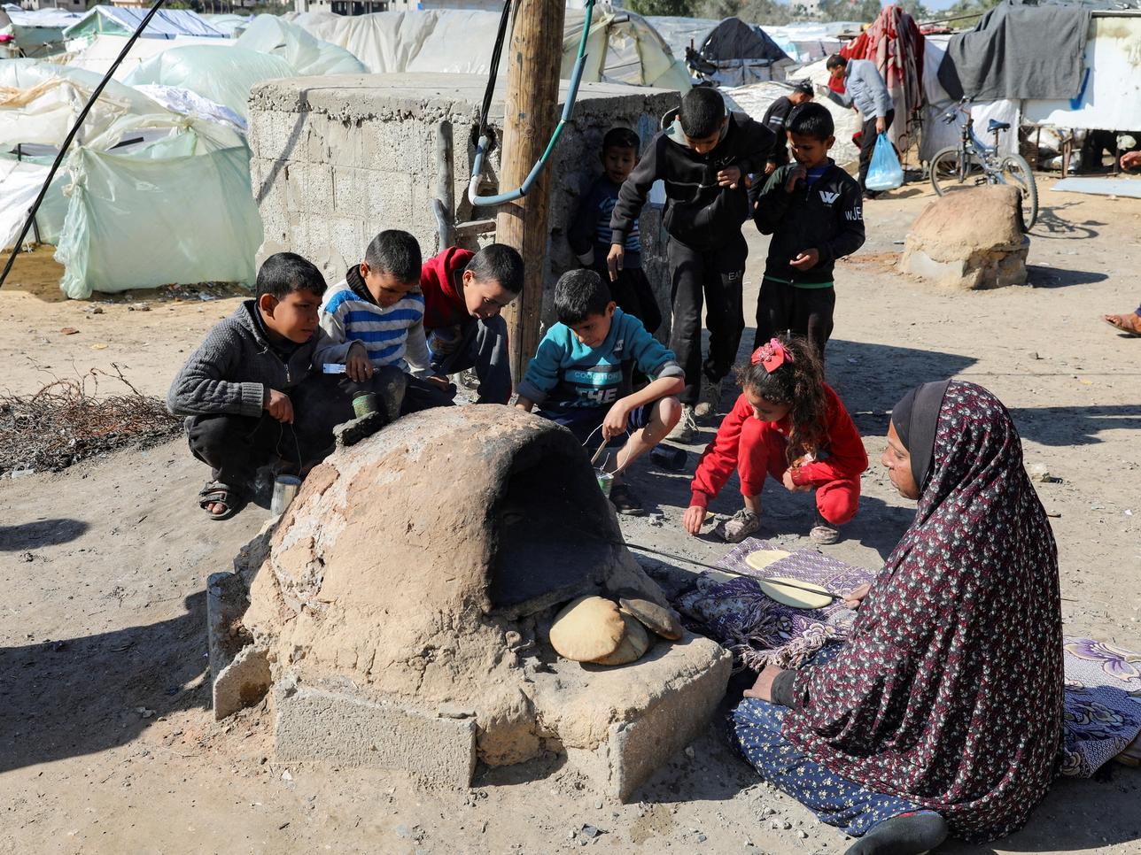 A Palestinian woman bakes bread as children sit next to her, while Gaza residents face crisis levels of hunger and soaring malnutrition.