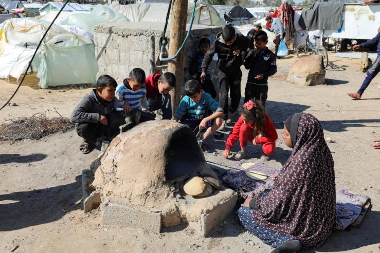 A Palestinian woman bakes bread as children sit next to her, while Gaza residents face crisis levels of hunger and soaring malnutrition.