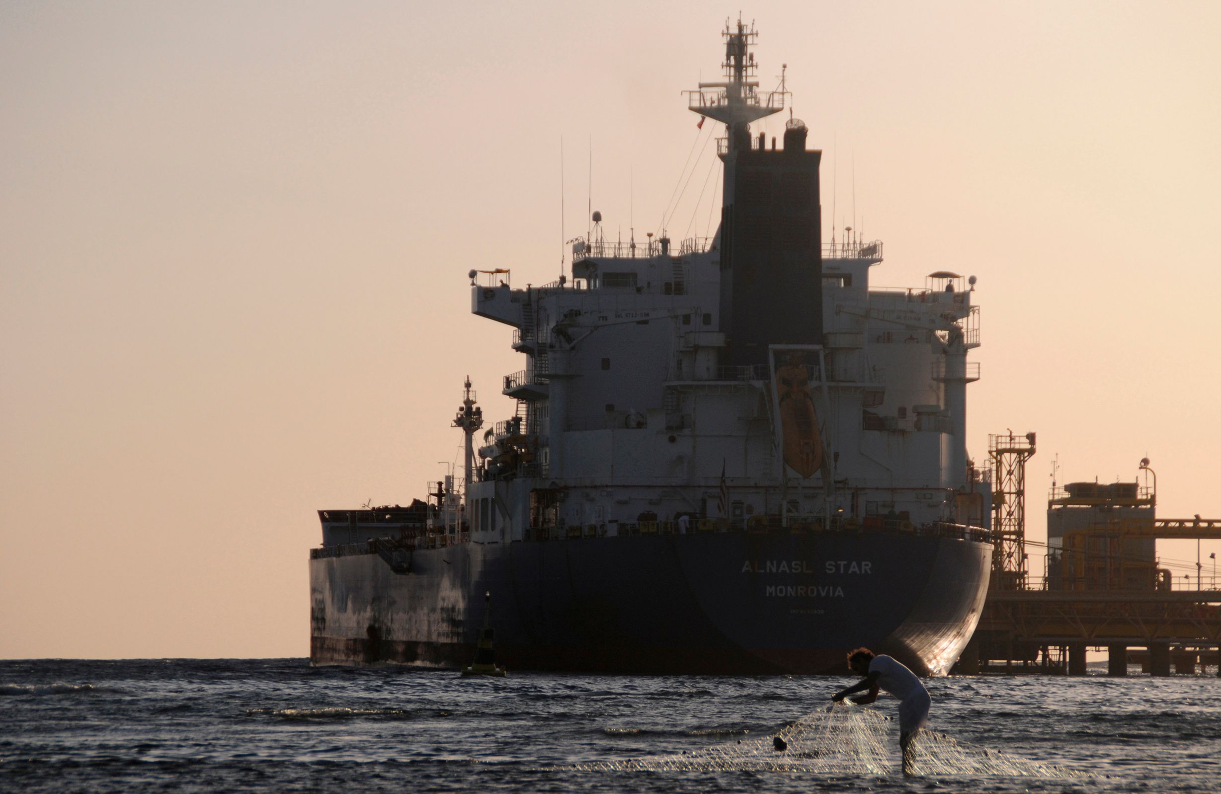 Fisherman pulls in his net as an oil tanker is seen at the port in the northwestern city of Duba.
