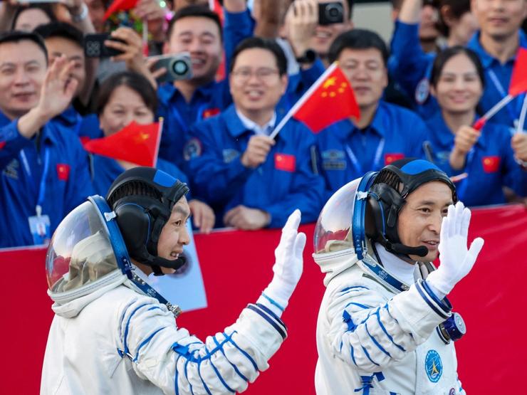 Chinese astronauts wave at people waving Chinese flags