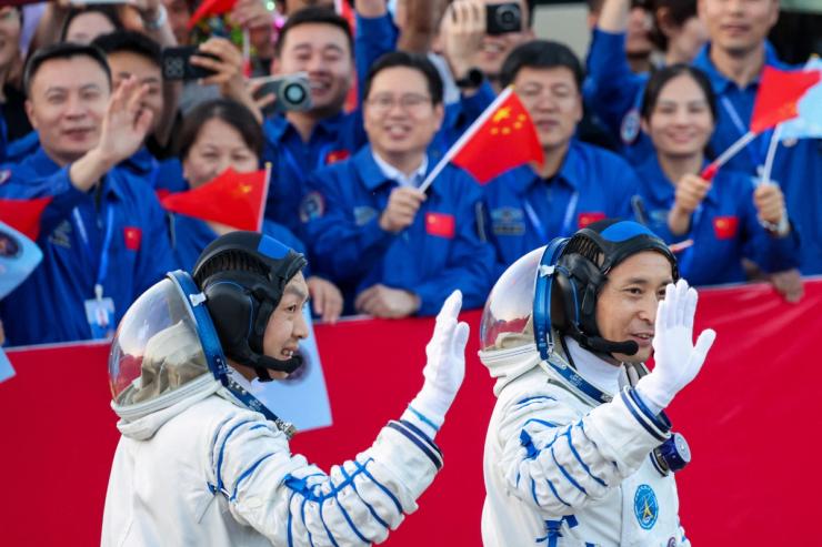 Chinese astronauts wave at people waving Chinese flags