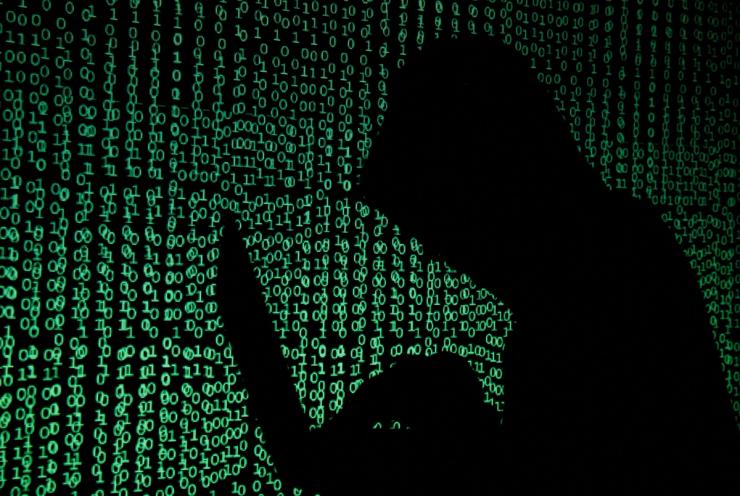Hooded man holds laptop computer as cyber code is projected on him in this illustration picture.