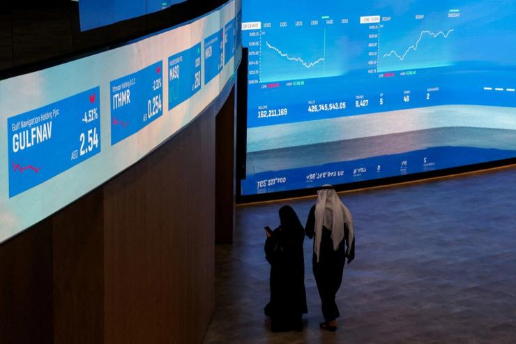 People walk near screens displaying stock information at the Dubai Financial Market