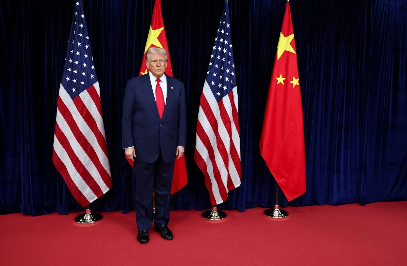 Trump standing next to US and Chinese flags.