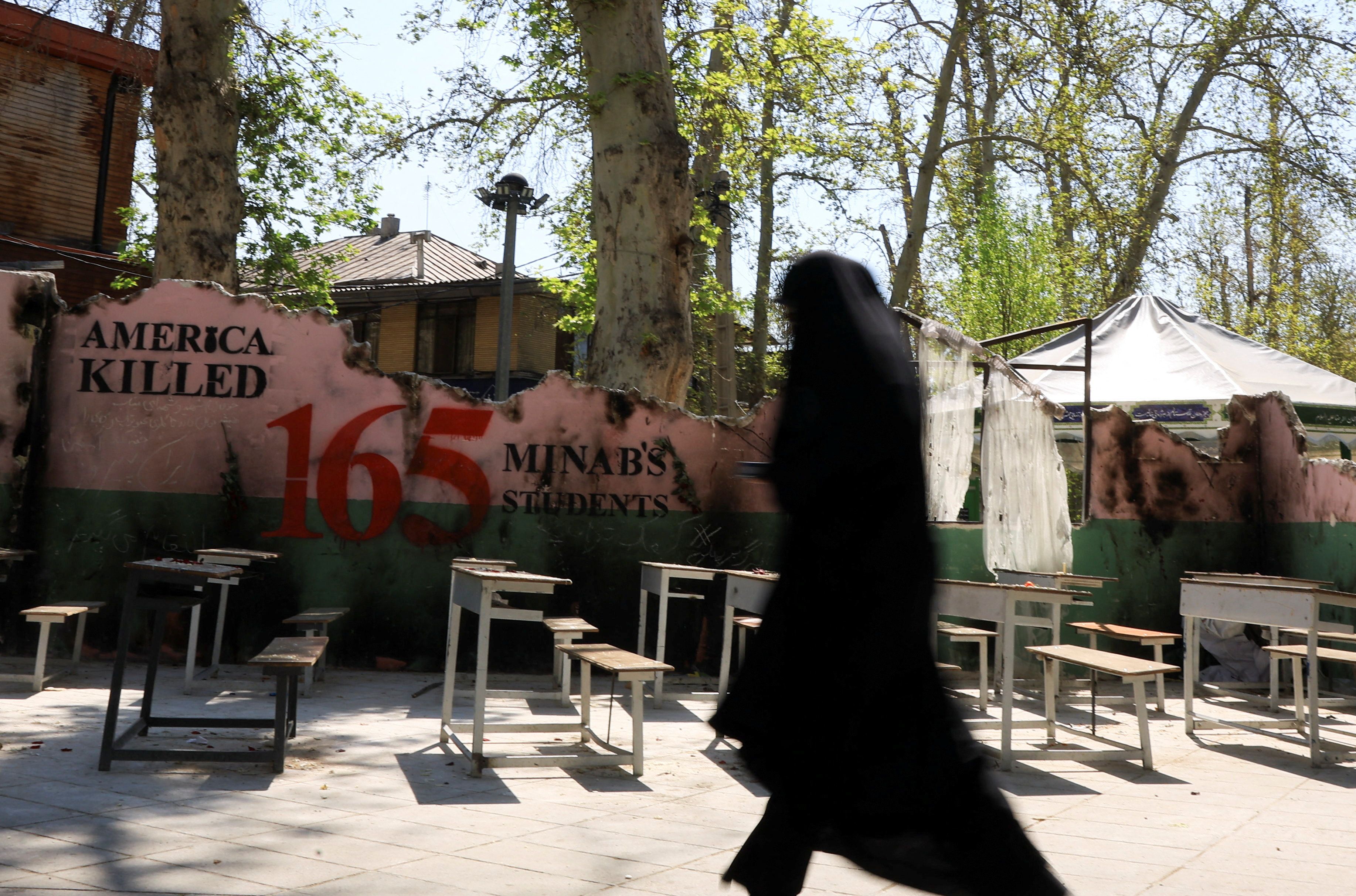 An Iranian woman walks past a monument for schoolchildren who were killed in a strike