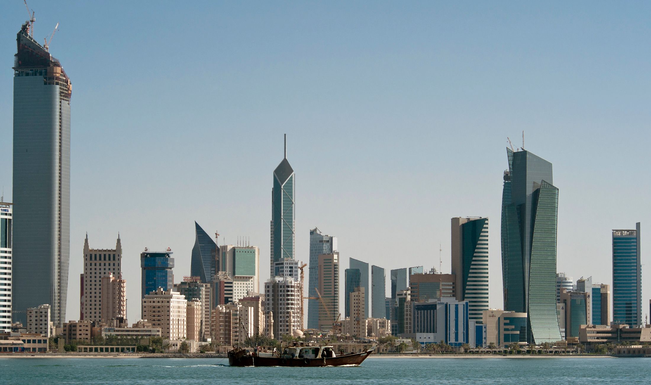 A fishing boat passes in front of the Kuwait City skyline.
