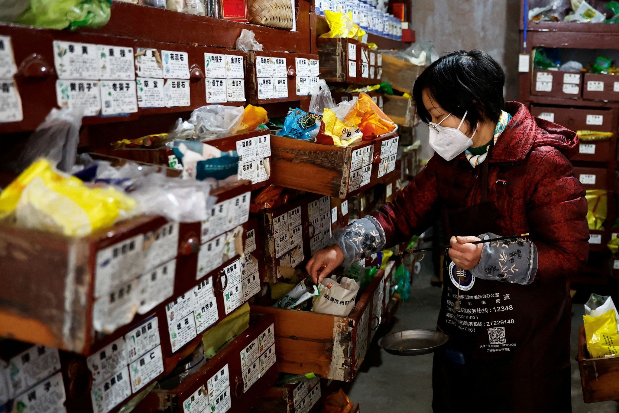 A pharmacist surnamed Wang, 57, weighs traditional Chinese medicine (TCM) herbs for a patient at a pharmacy 