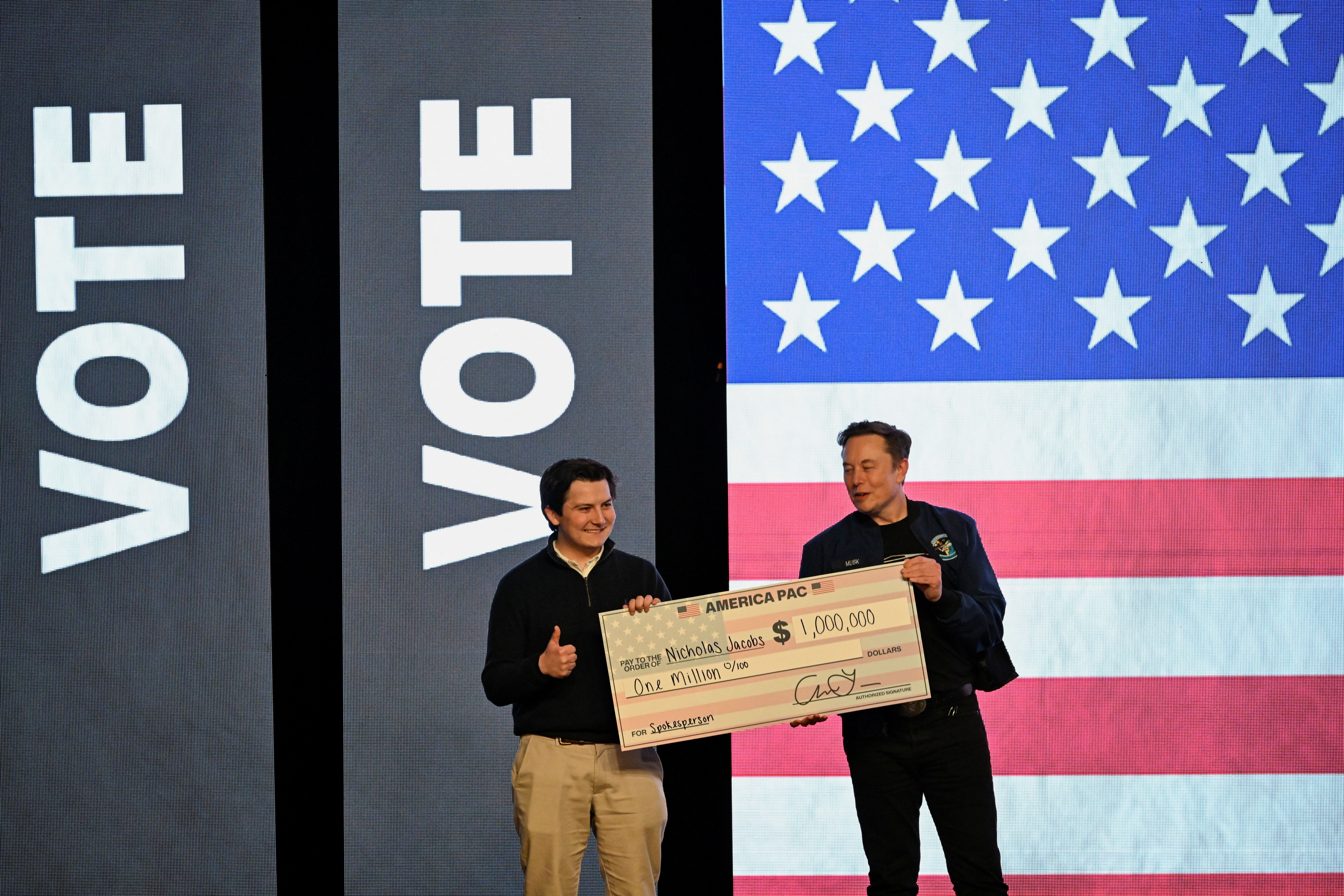 Elon Musk gives a check to an audience member during a rally in support of a conservative state Supreme Court candidate.