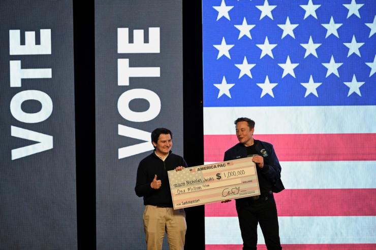 Elon Musk gives a check to an audience member during a rally in support of a conservative state Supreme Court candidate.