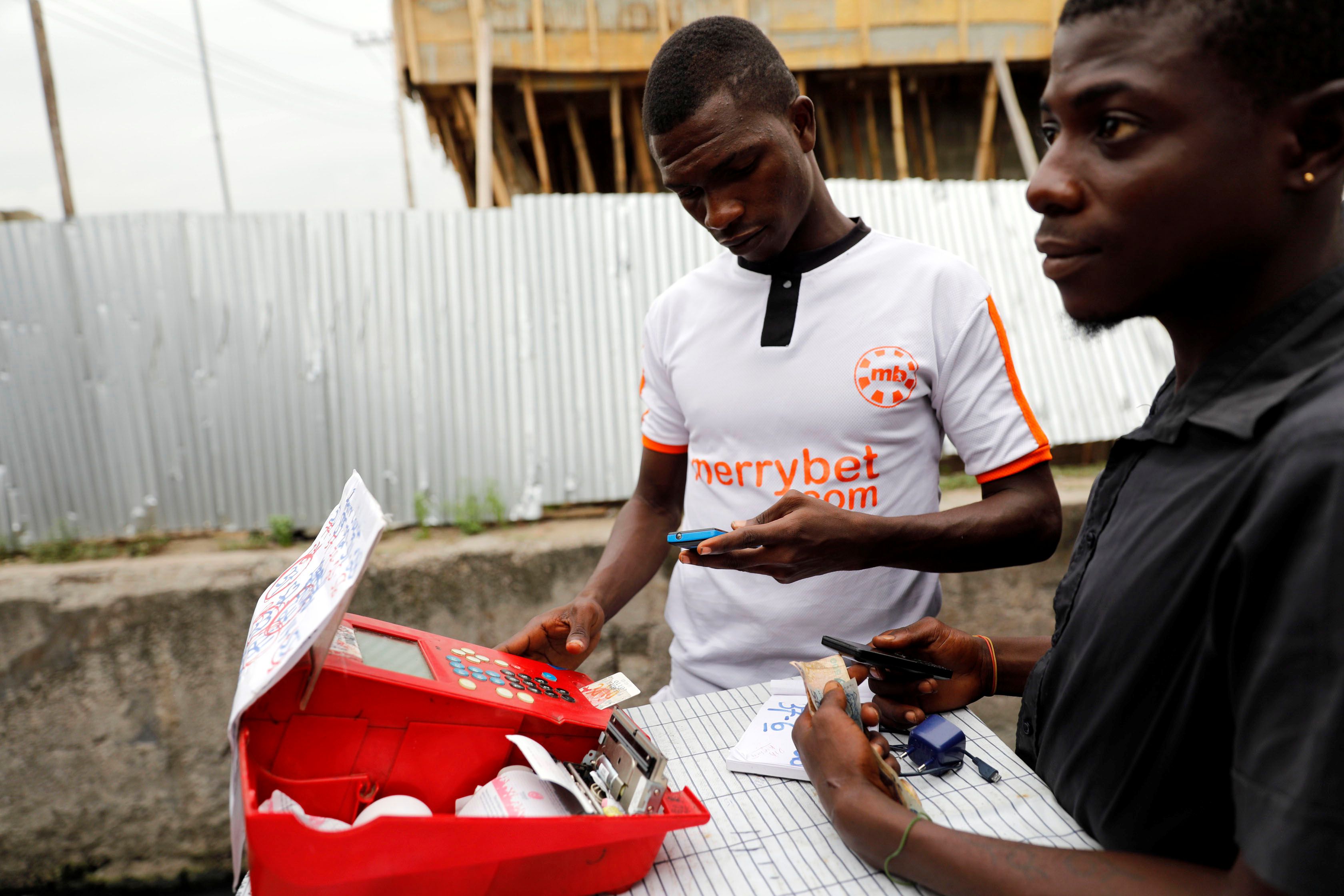 A bet player uses a machine and mobile phone for betting at a roadside betting kiosk in Ojuelegbe district in Lagos, Nigeria.