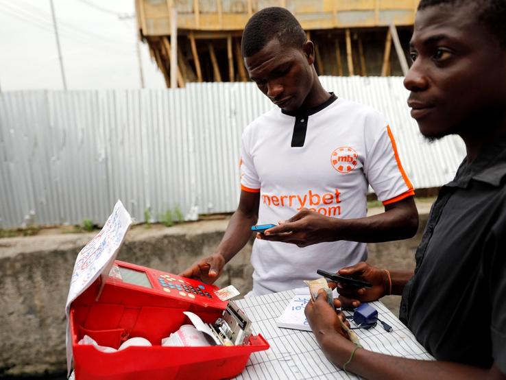A bet player uses a machine and mobile phone for betting at a roadside betting kiosk in Ojuelegbe district in Lagos, Nigeria.