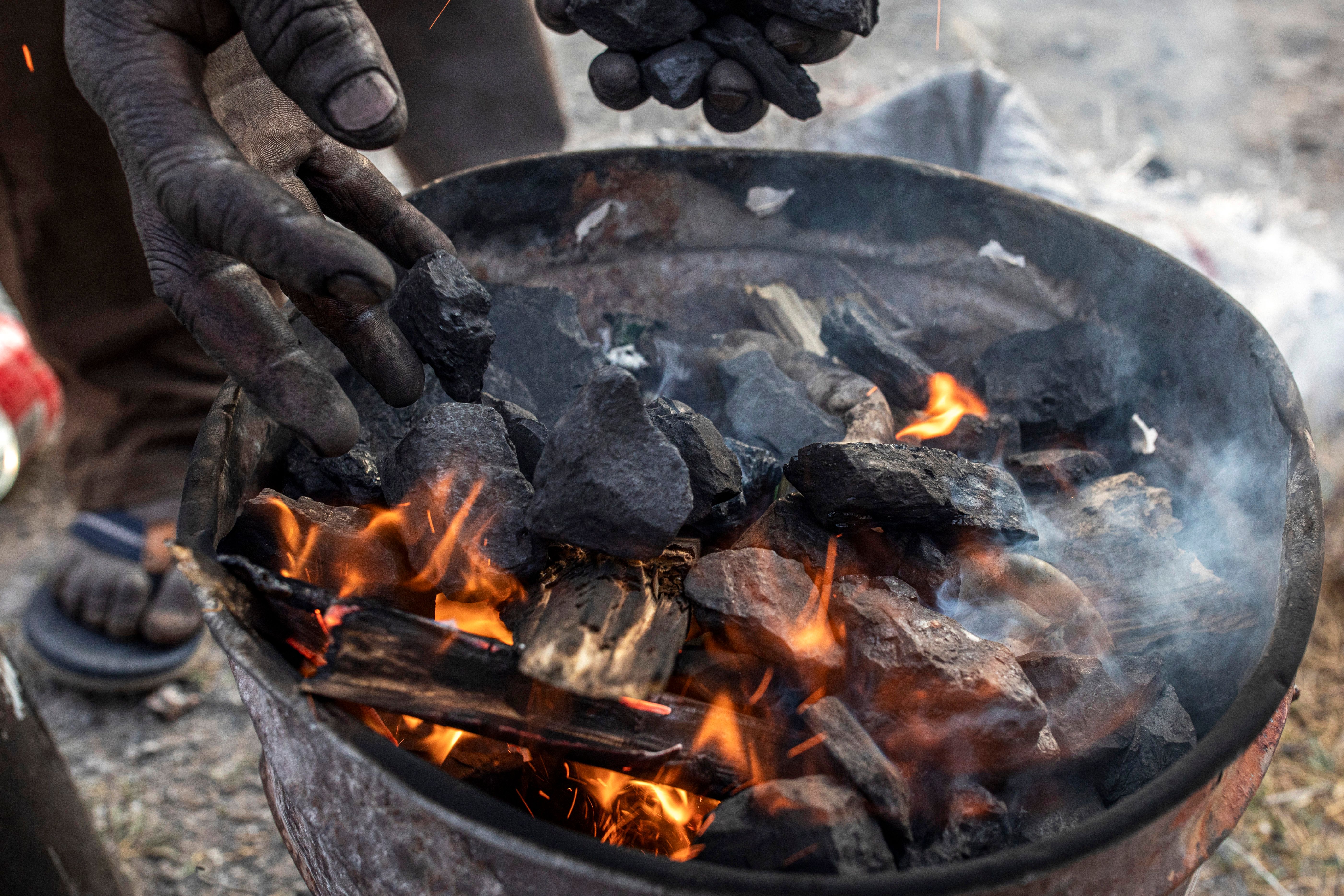 Salvador Neves starts a fire with coal before cooking on September 22, 2024, in Komati, Mpumalanga Province, South Africa.