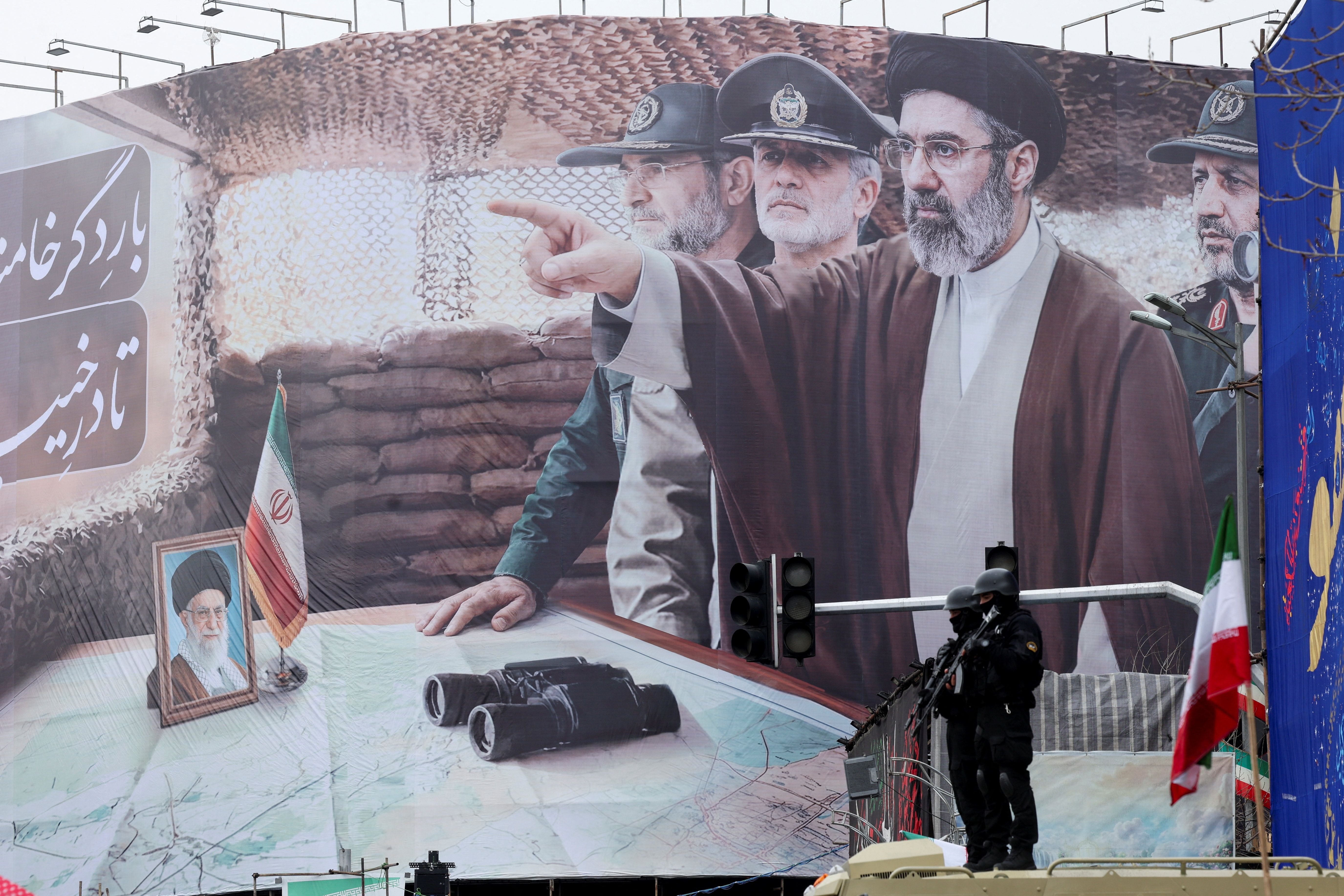 Security personnel stand guard in front of a banner with an image of Iran’s new Supreme Leader Mojtaba Khamenei 
