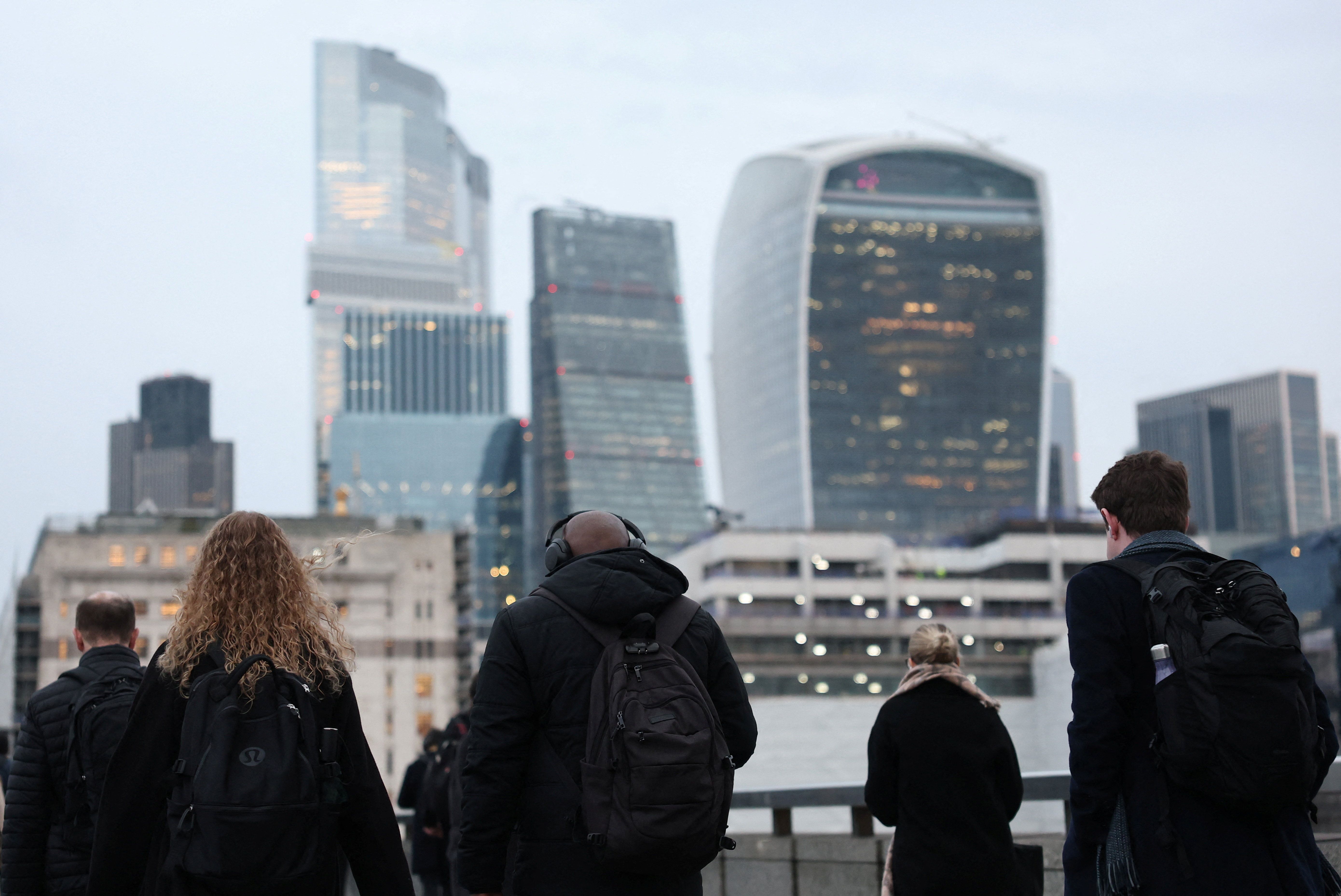 Workers cross London Bridge during the morning rush-hour with skyscrapers of the City of London financial district seen behind