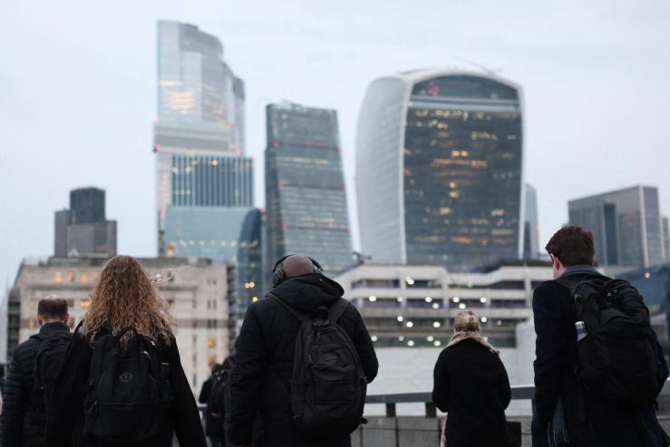 Workers cross London Bridge during the morning rush-hour with skyscrapers of the City of London financial district seen behind