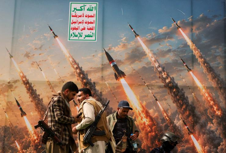 Two Houthi supporters stand in front of a picture of missiles in the sky.