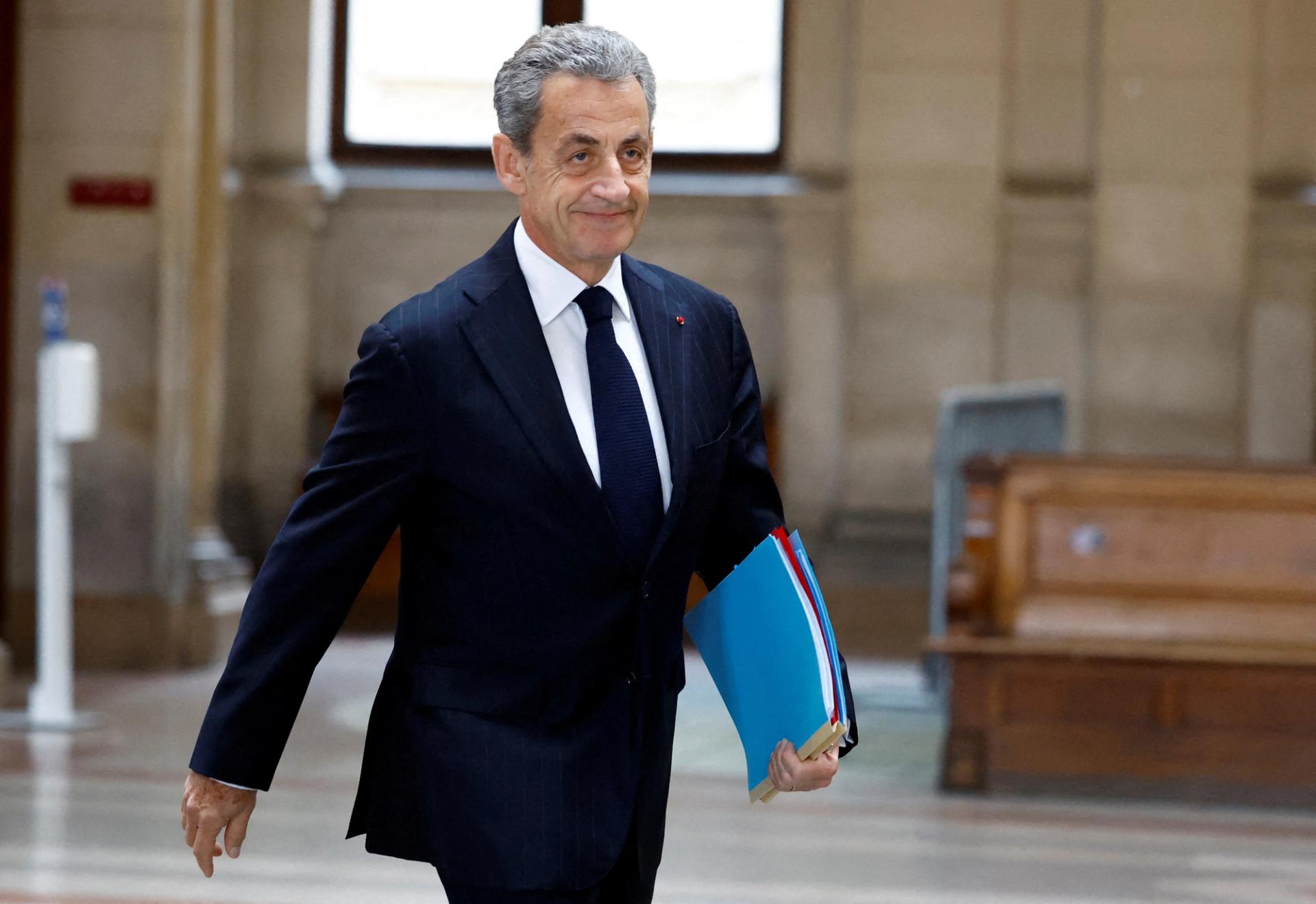 Nicolas Sarkozy, wearing a dark suit and tie and carrying a stack of documents, arrives for a hearing at his appeal trial in Paris