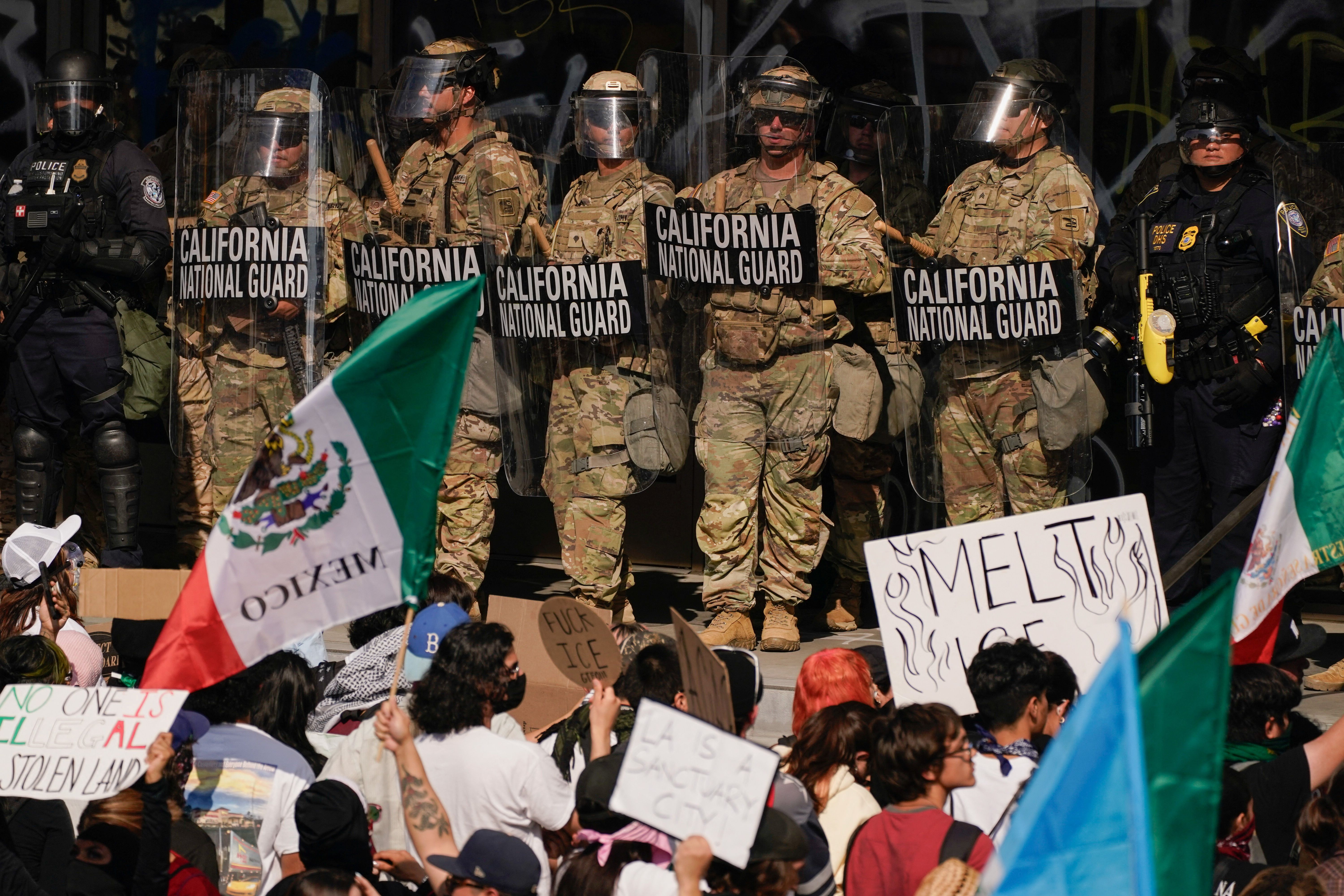 California National Guard troops and police officers stand guard as people attend a rally against federal immigration sweeps.