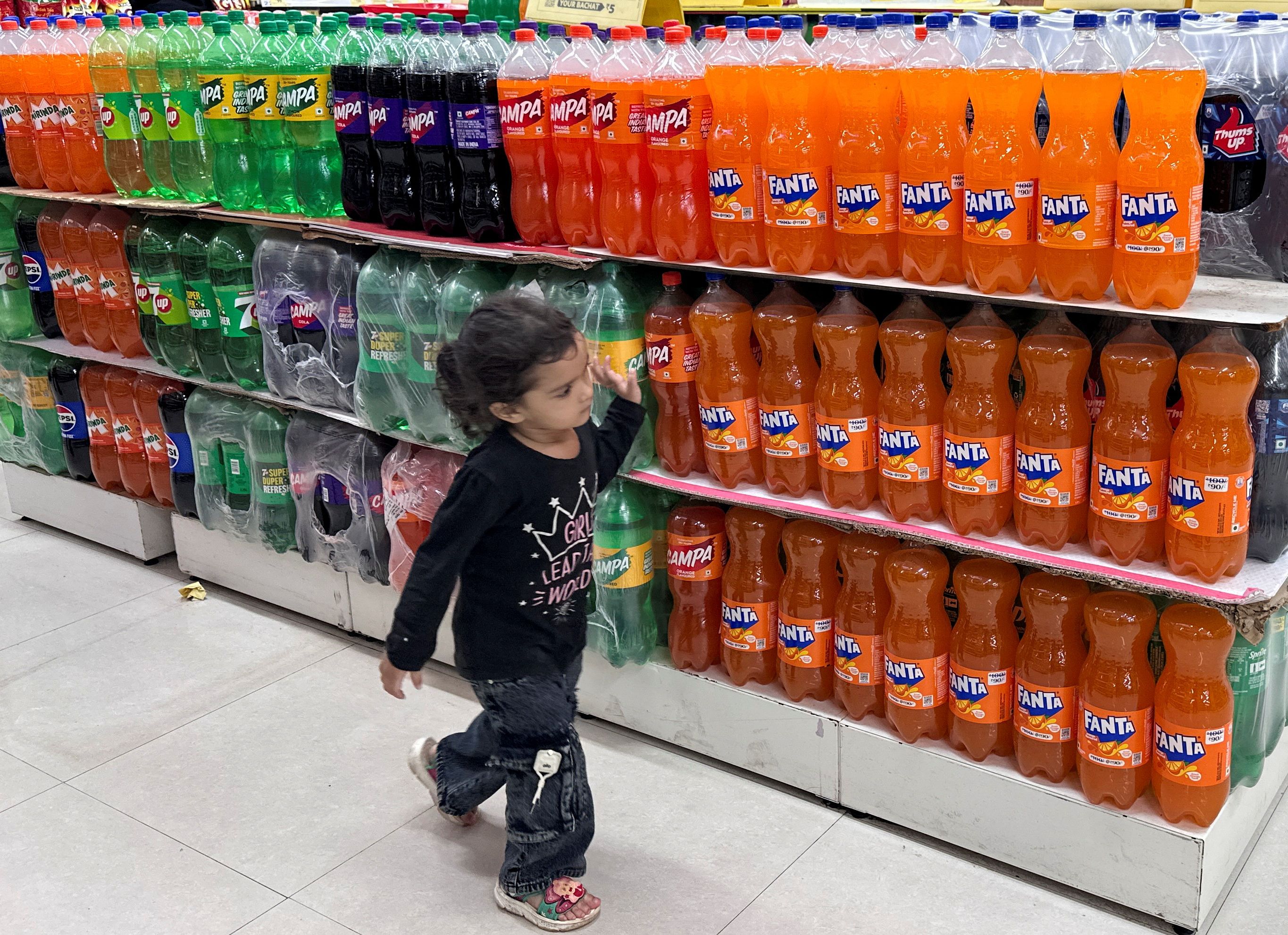 A little girl walks past bottles of soda in a store in Mumbia, India