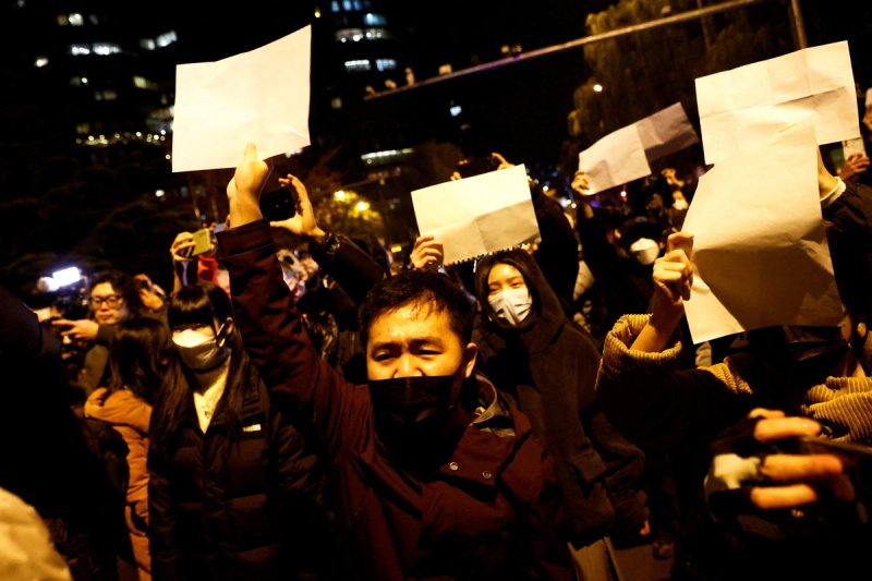 People gather for a vigil and hold white sheets of paper in protest of coronavirus disease (COVID-19) restrictions, as they commemorate the victims of a fire in Urumqi, as outbreaks of the coronavirus disease continue in Beijing, China.
