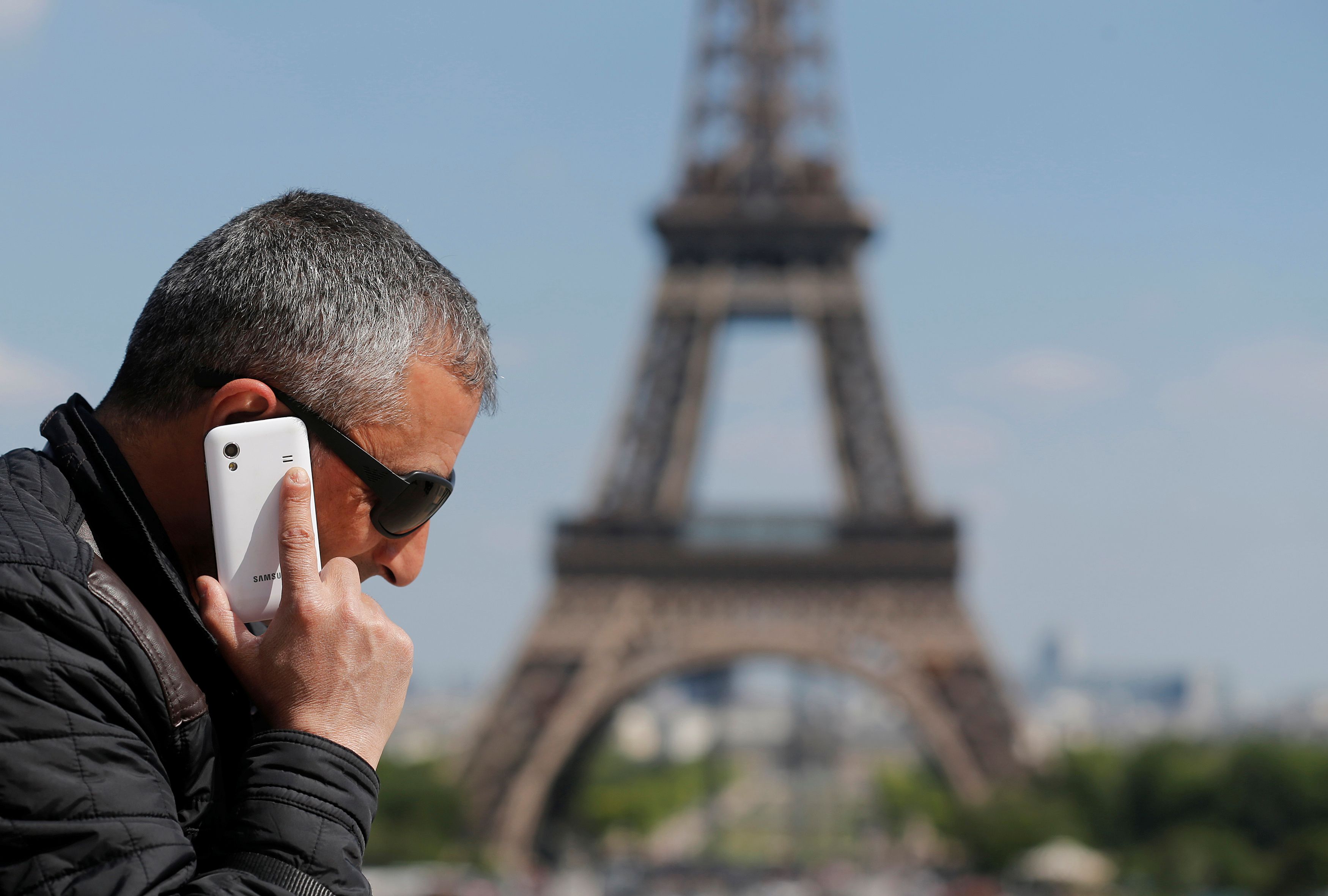 A man uses a phone near the Eiffel Tower