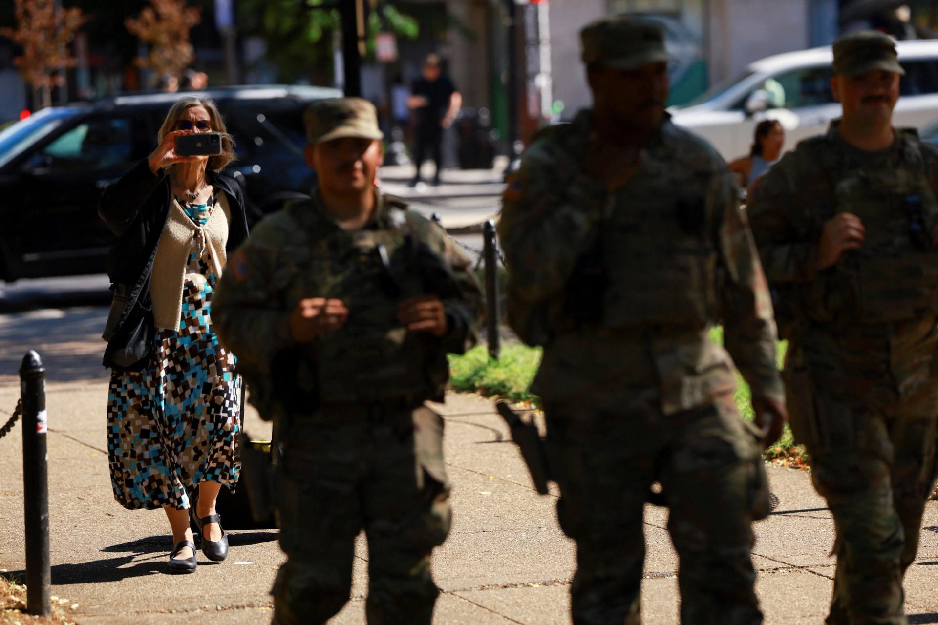 A woman uses her phone to capture the scene as members of the South Carolina National Guard carrying their firearms patrol Dupont Circle neighborhood in Washington, DC.