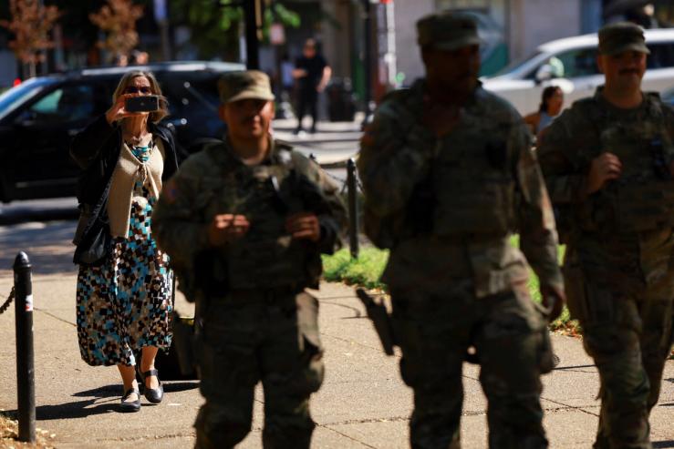 A woman uses her phone to capture the scene as members of the South Carolina National Guard carrying their firearms patrol Dupont Circle neighborhood in Washington, DC.