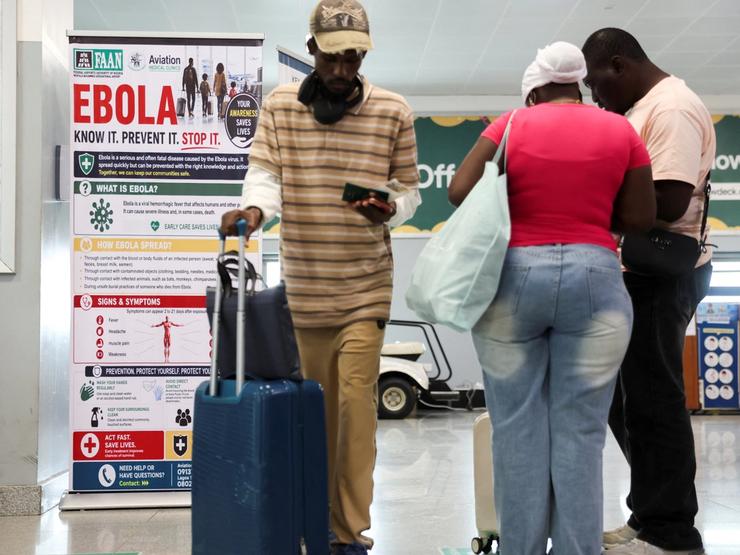 Travellers next to a banner displayed by a health screening station at Murtala Muhammed International Airport.