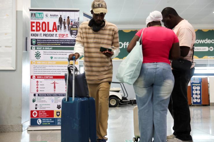 Travellers next to a banner displayed by a health screening station at Murtala Muhammed International Airport.