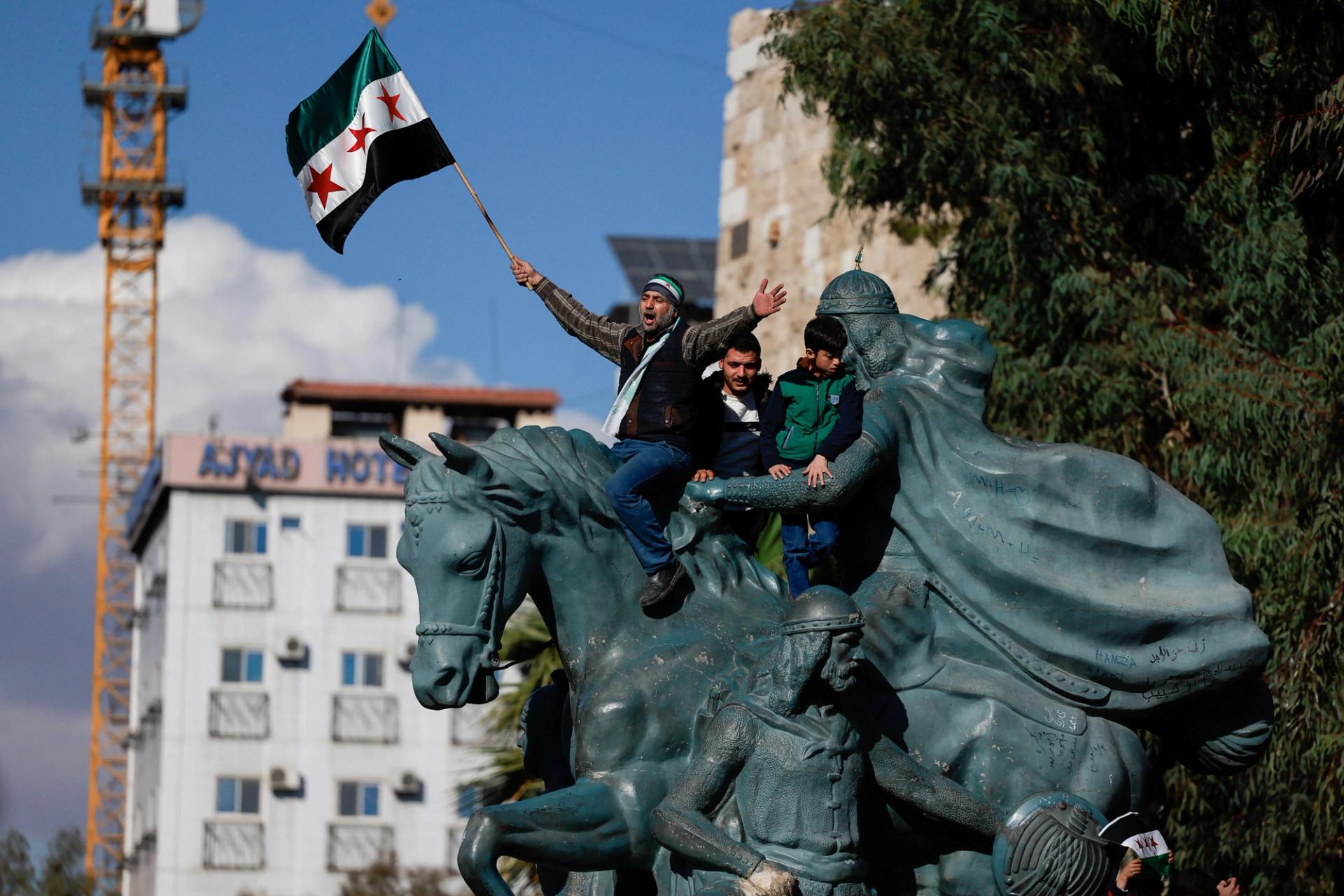 A man waves the flag adopted by the new Syrian rulers on a statute of Saladin in Damascus