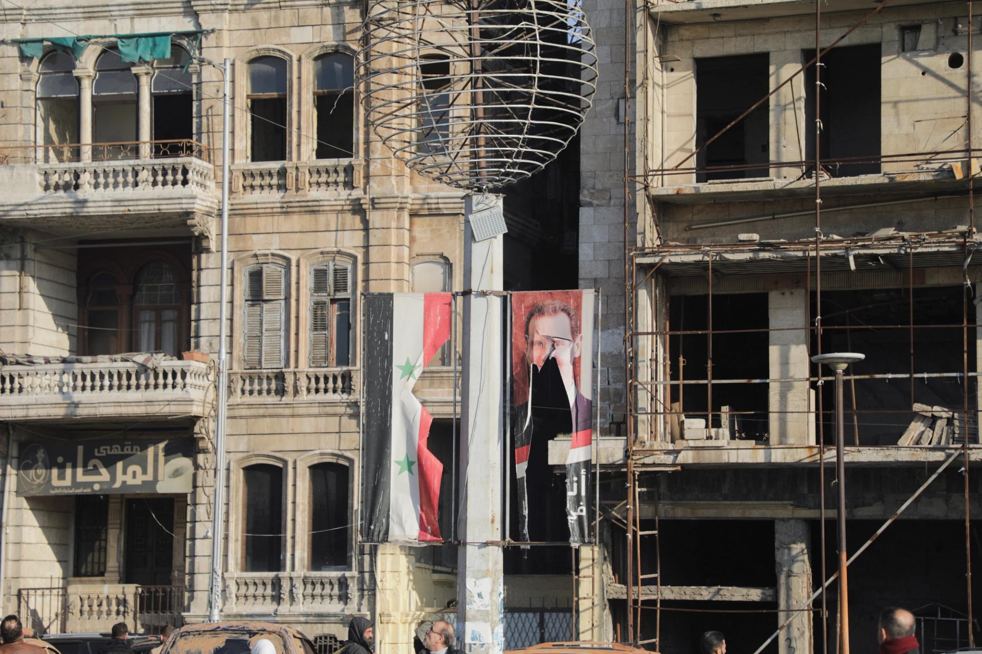 People stand near a ripped poster of Syria’s Bashar al-Assad in Aleppo