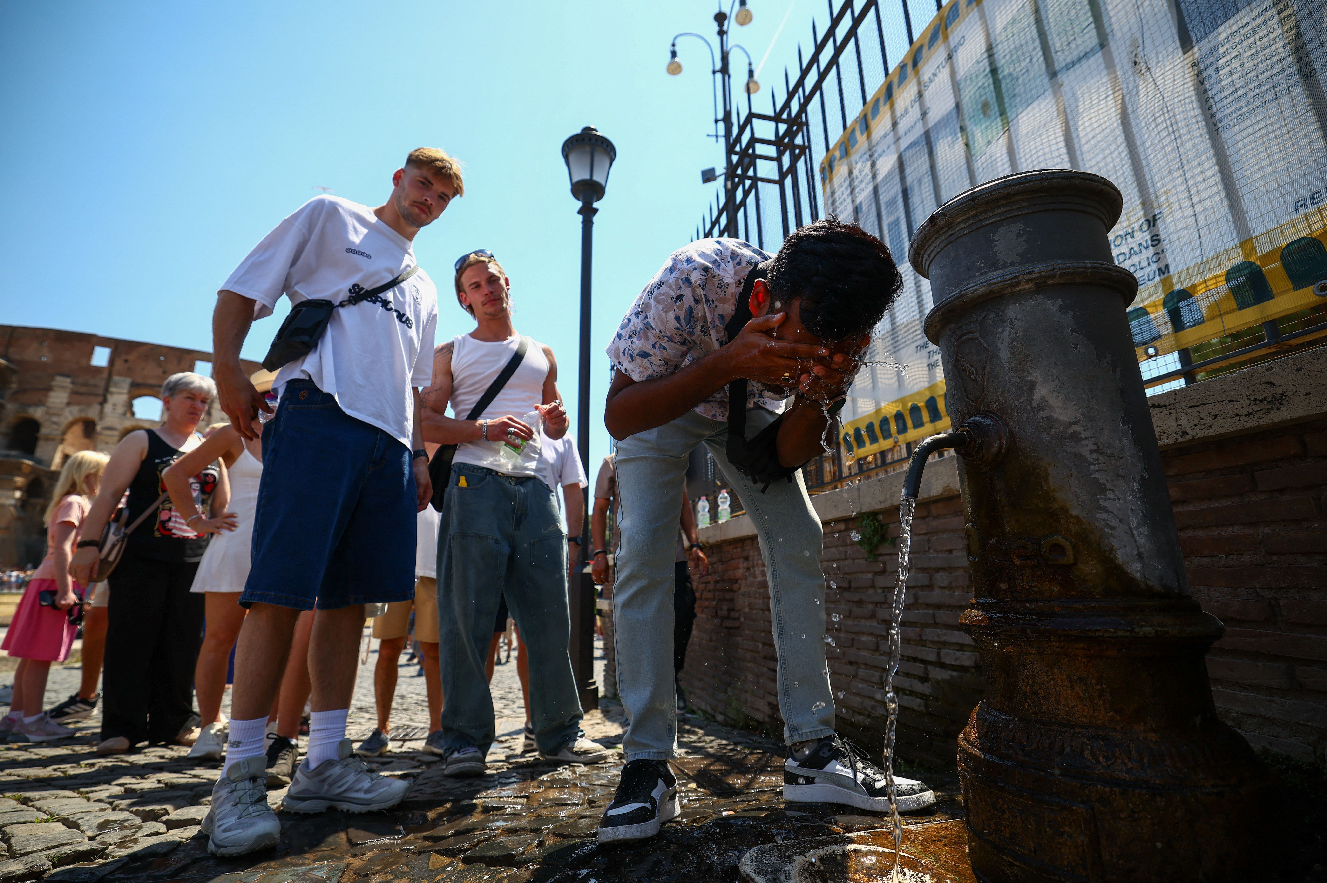 A person cools off from a public fountain near the Colosseum during a heatwave in Rome