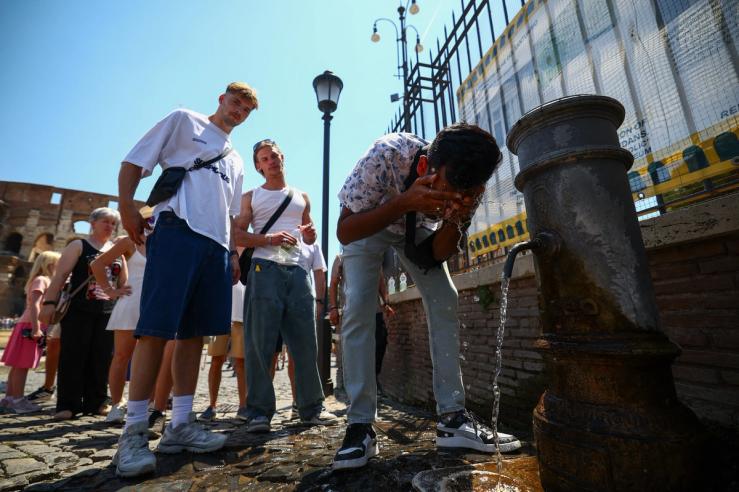 A person cools off from a public fountain near the Colosseum during a heatwave in Rome