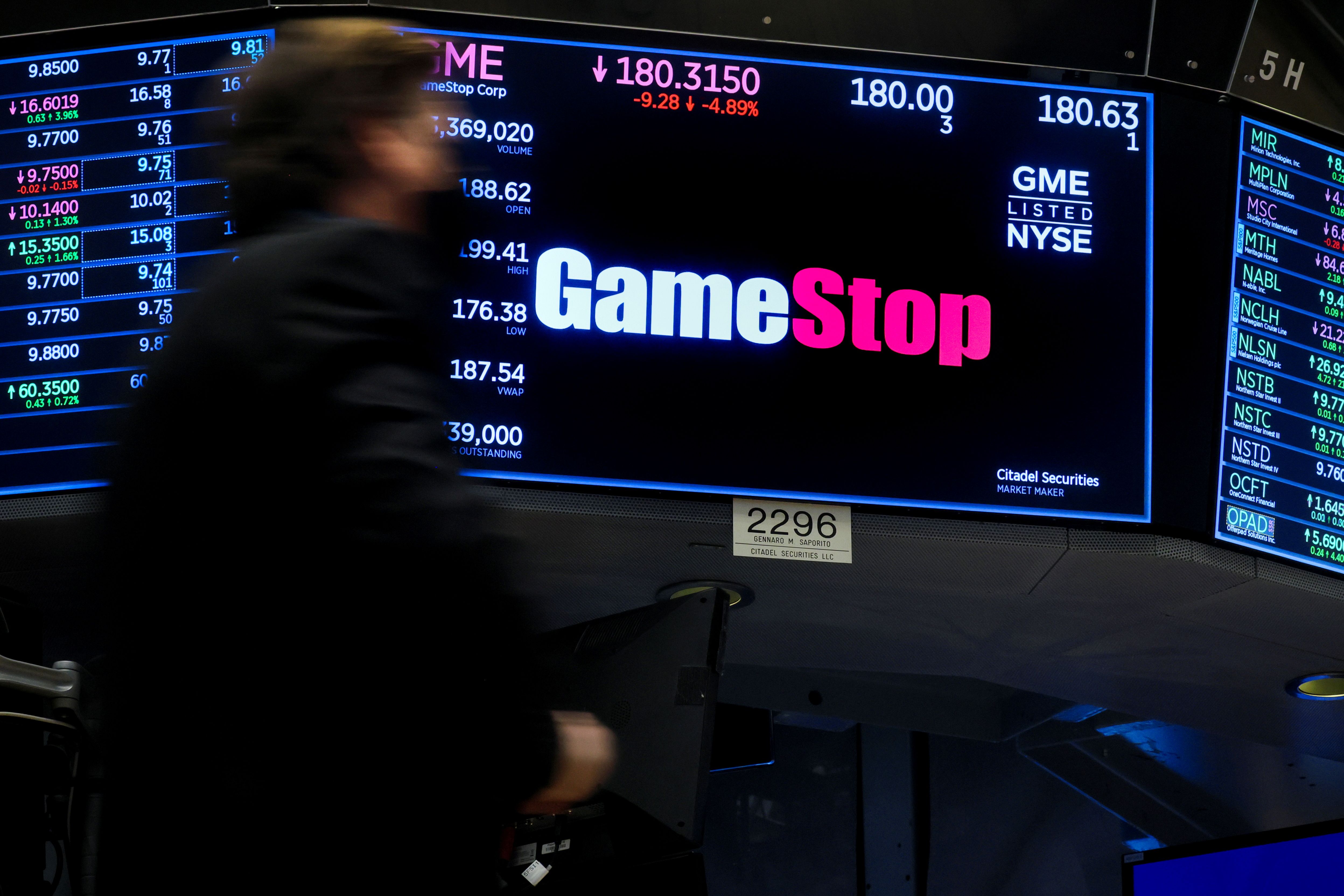 A screen displays the logo and trading information for GameStop on the floor of the New York Stock Exchange.