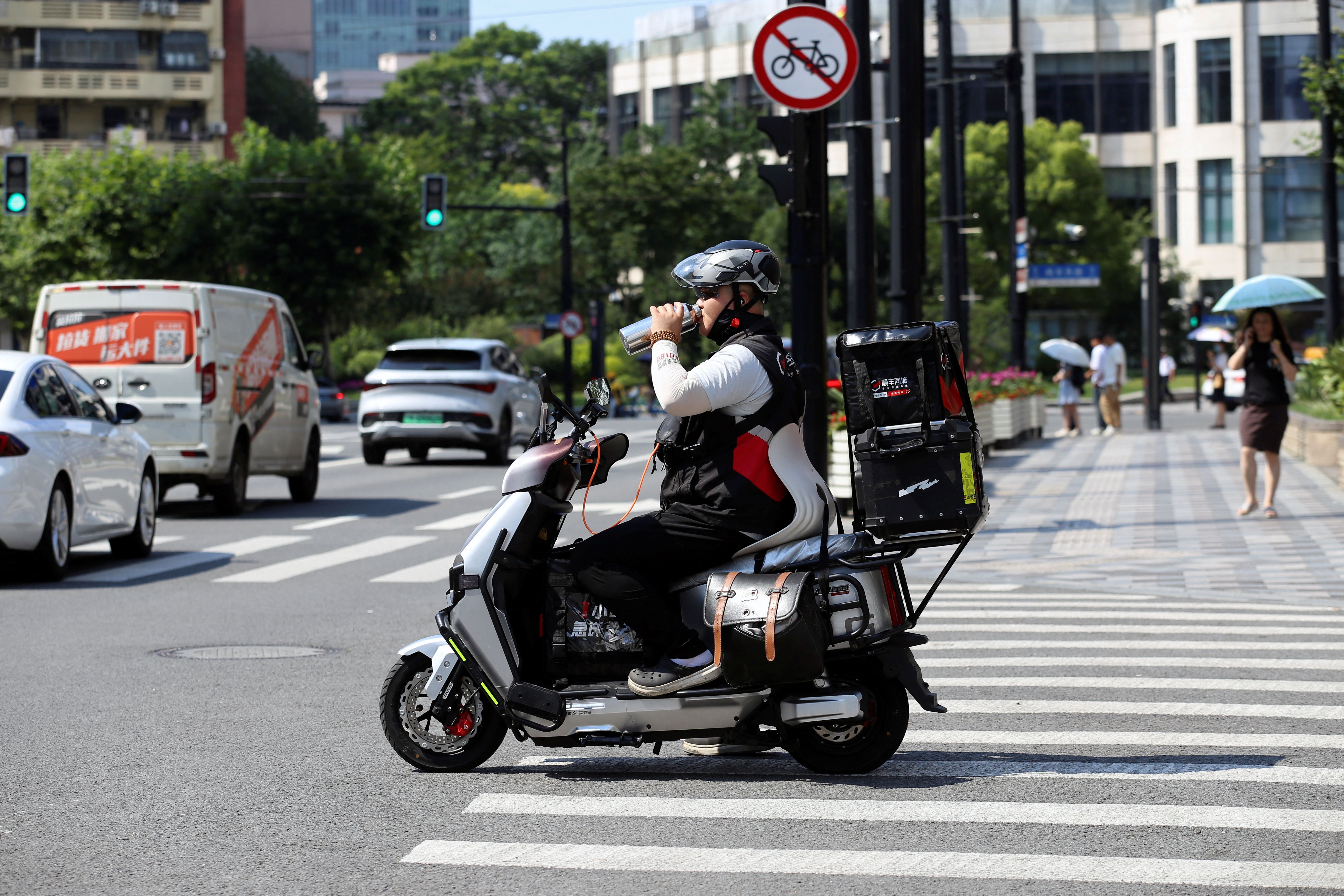 A delivery driver drinks from a bottle at an intersection in Shanghai