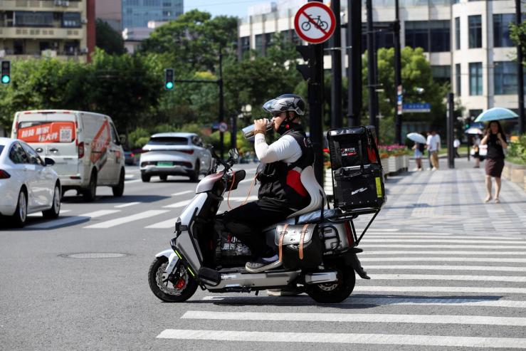 A delivery driver drinks from a bottle at an intersection in Shanghai