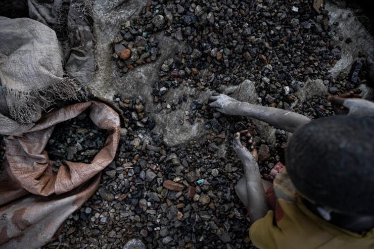A young person sifts through stones at a cobalt and copper mining pit .