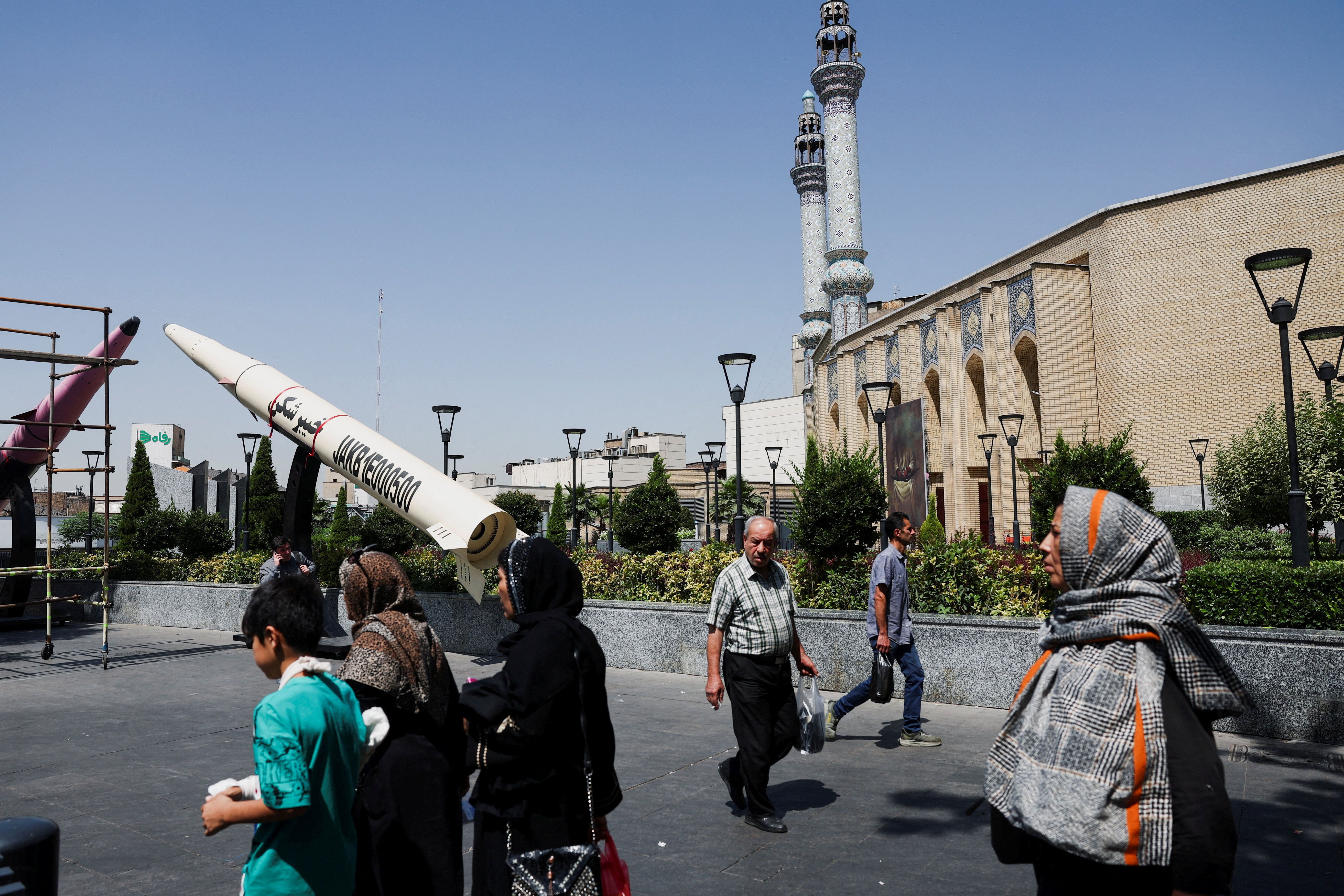 People walk next to a symbolic mock-up of an Iranian missile, on a street in Tehran.