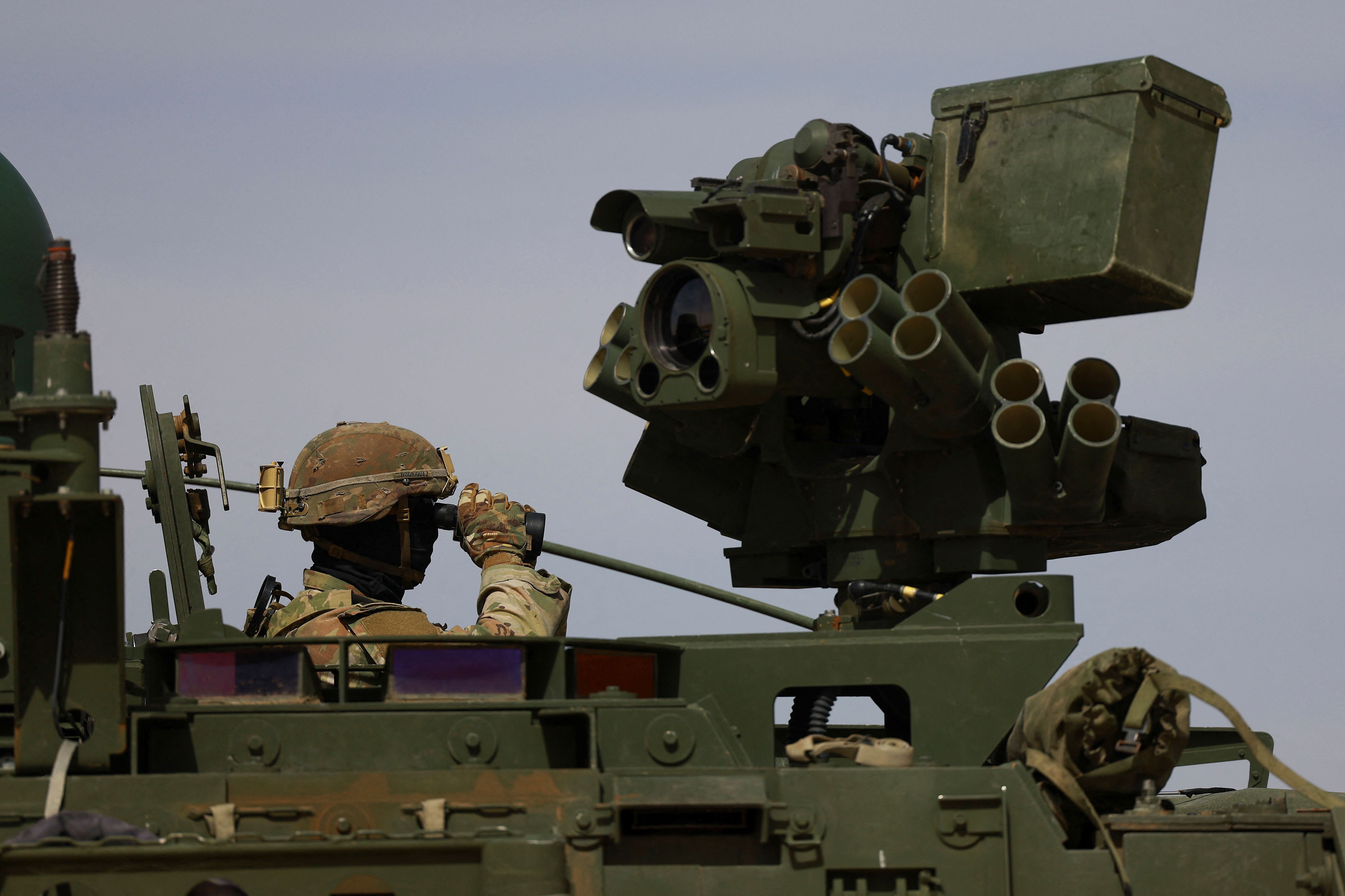 A US Army member looks through binoculars aboard an armored vehicle at the US-Mexico border. 