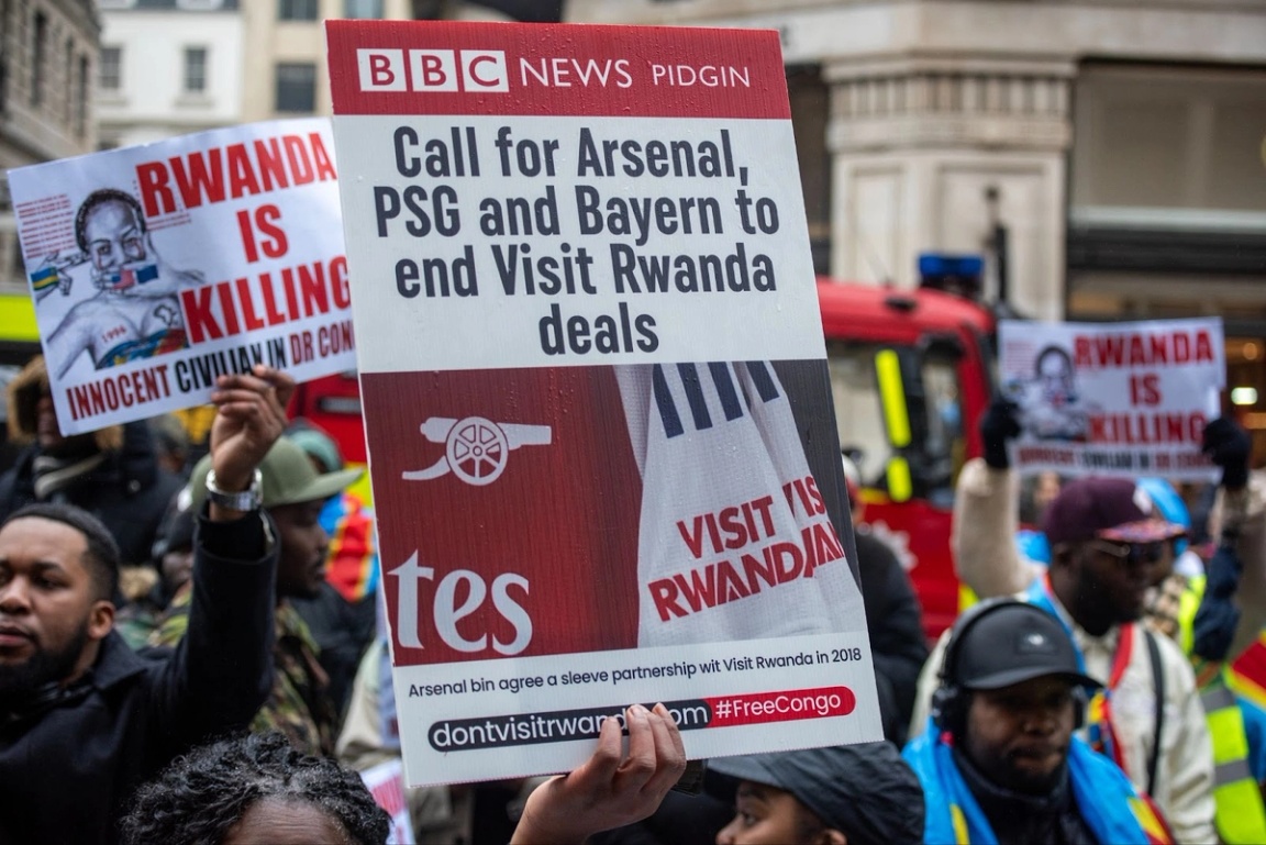 A protester holds a placard to demand that football teams Arsenal, Bayern Munich, and Paris Saint-Germain stop ‘Visit Rwanda’ deals.