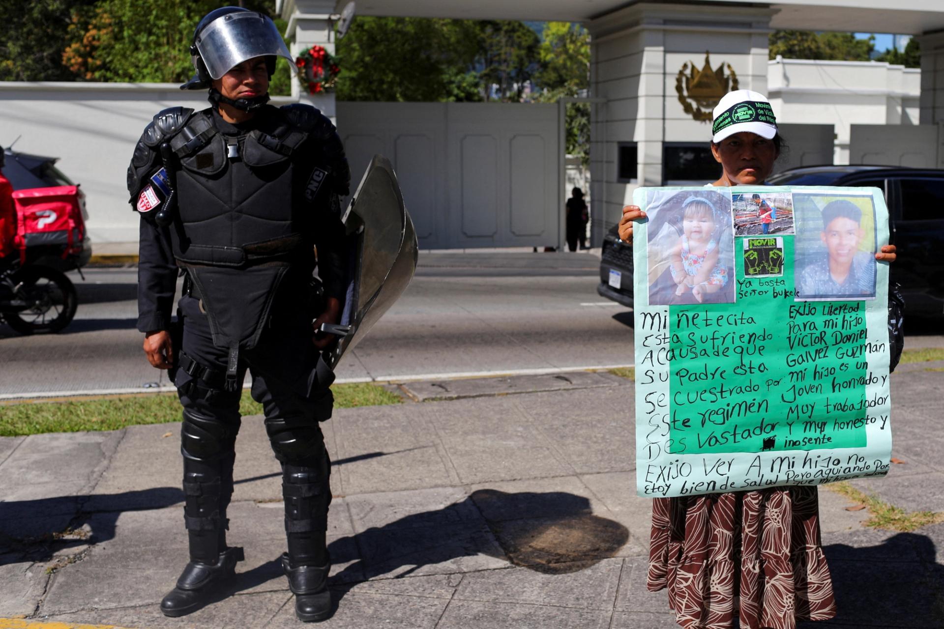 A police officer stands next to a woman protesting the detainment of people by the government as part of it’s battle against gang violence.