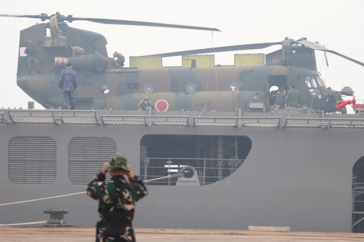 An Indonesian military member stands guard as Japanese military personnel stand near a Chinook helicopter.