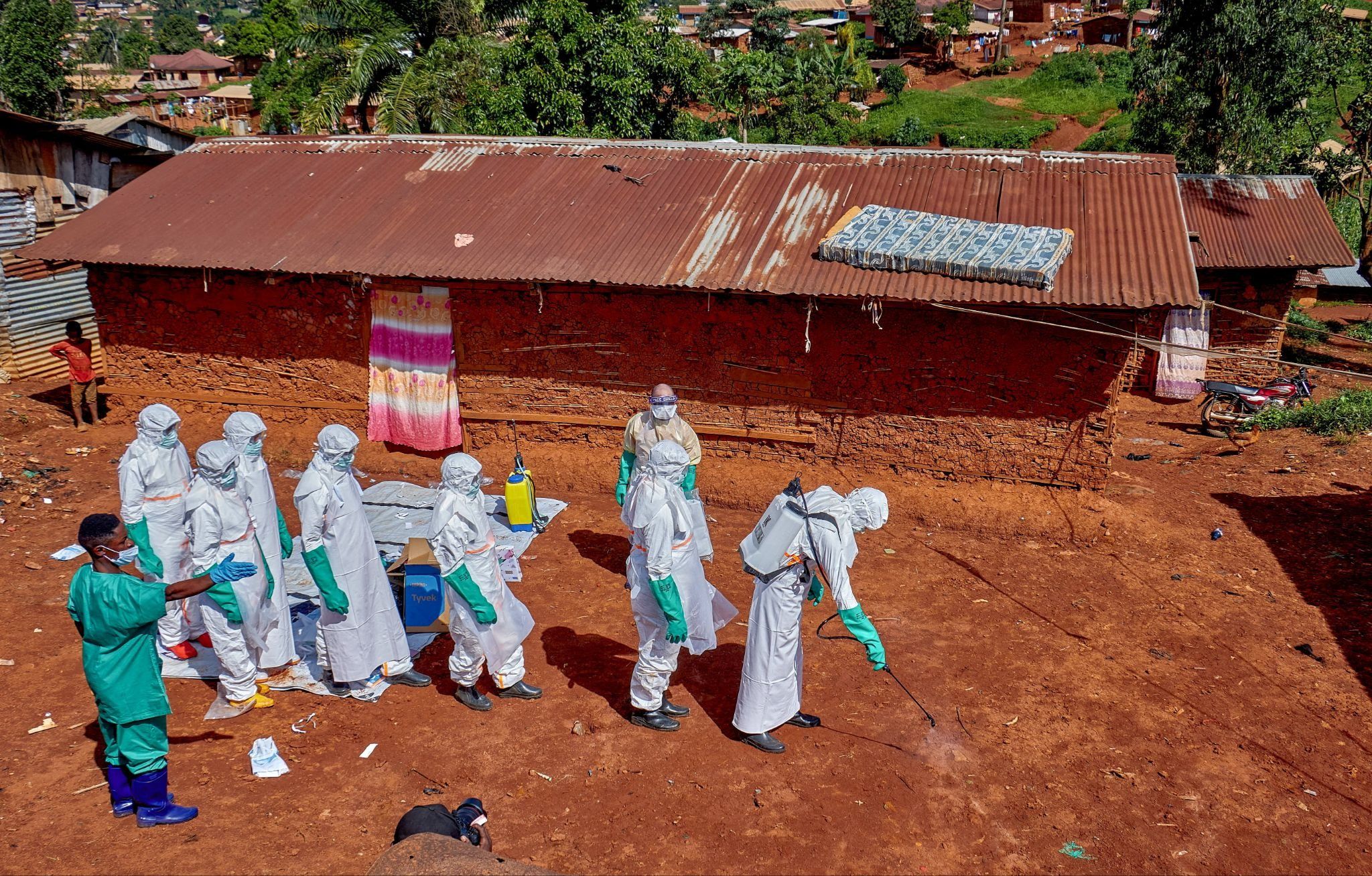 Red Cross workers wearing personal protective equipment walk in a formation as they disinfect the ground outside the house of an unidentified man who died of Ebola. 